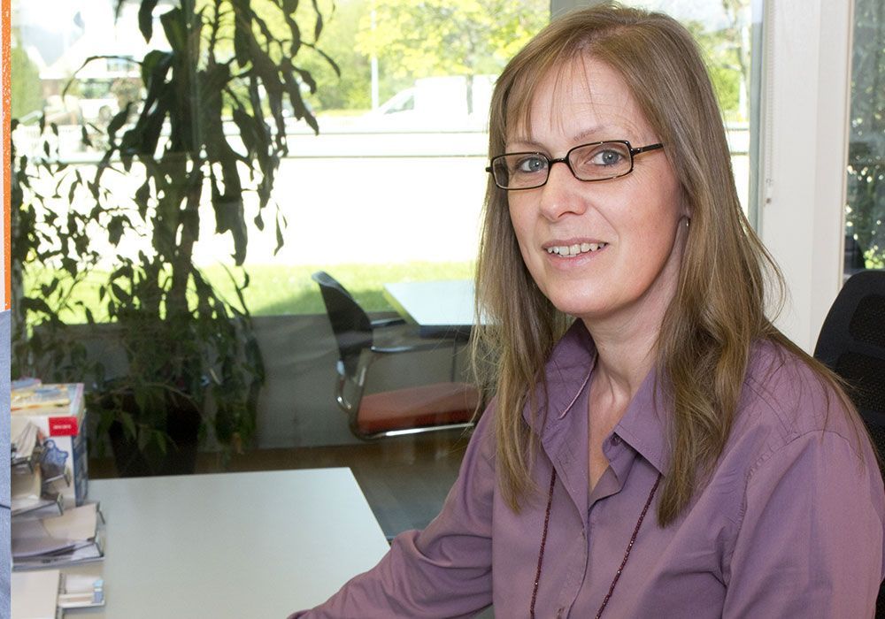 Eine Frau mit Brille sitzt an einem Schreibtisch vor einem Fenster