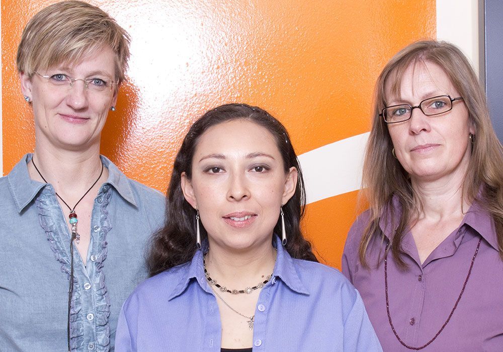 Drei Frauen posieren für ein Foto vor einer orangefarbenen Wand