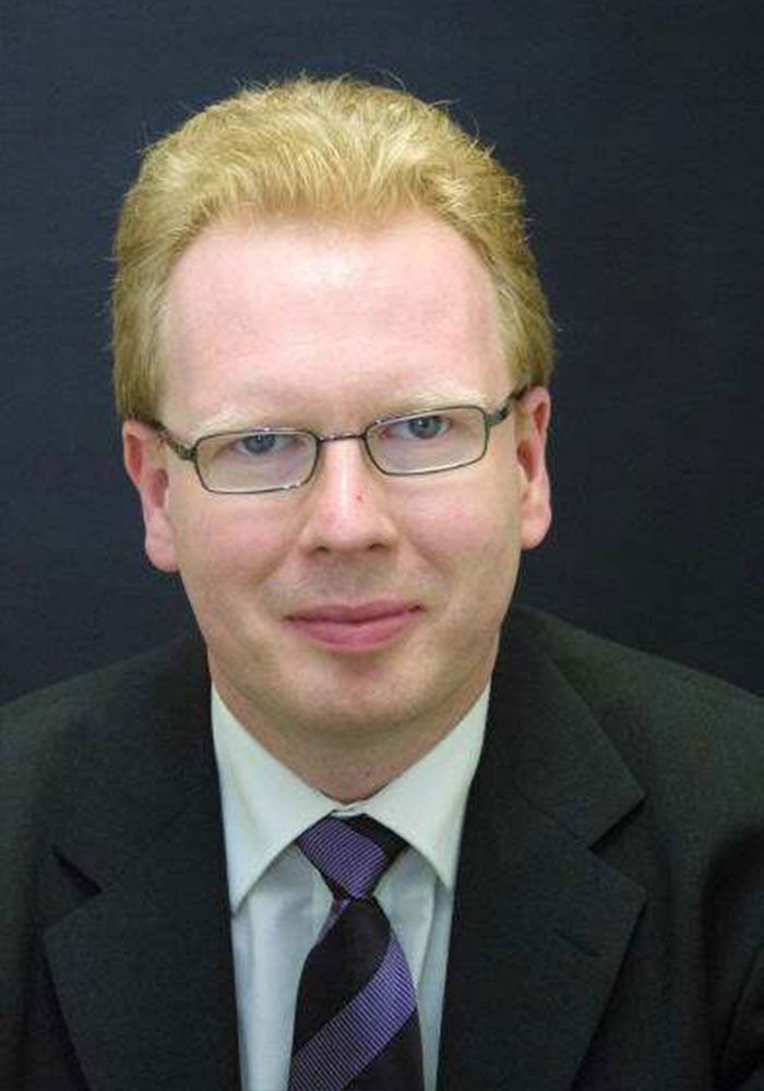 Ein Mann in Anzug und Krawatte trägt eine Brille.