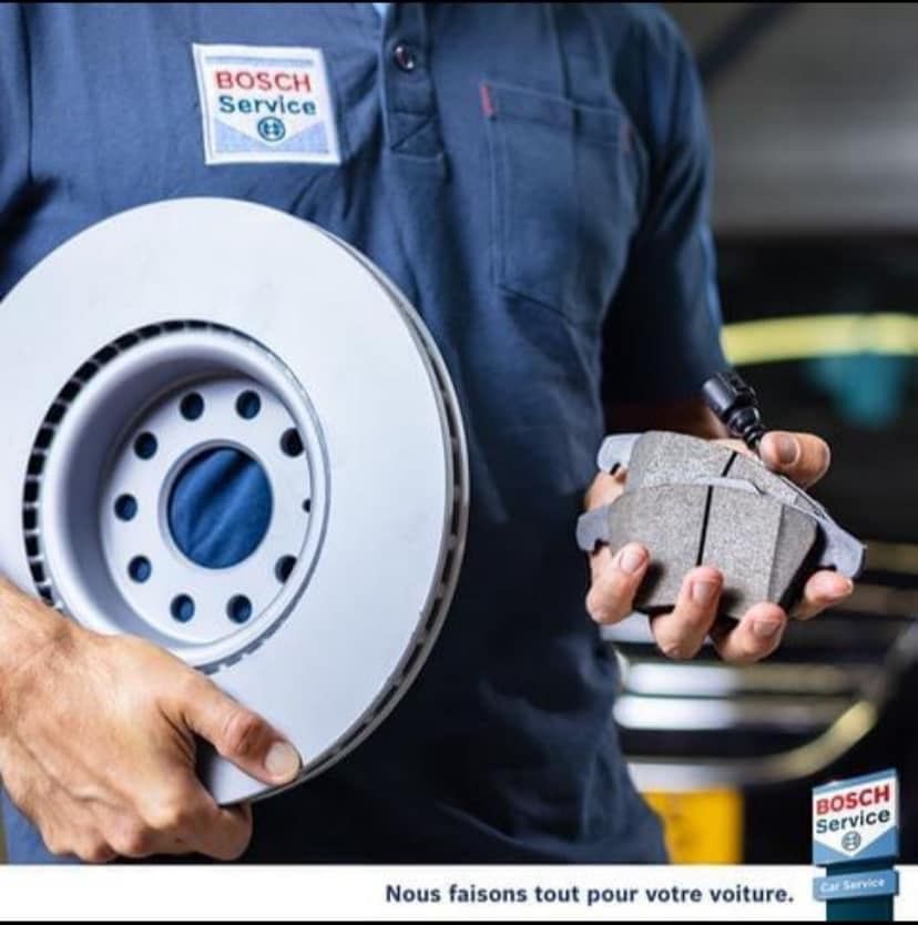 Un mécanicien tient un disque de frein et des plaquettes de frein dans un garage Bosch Service
