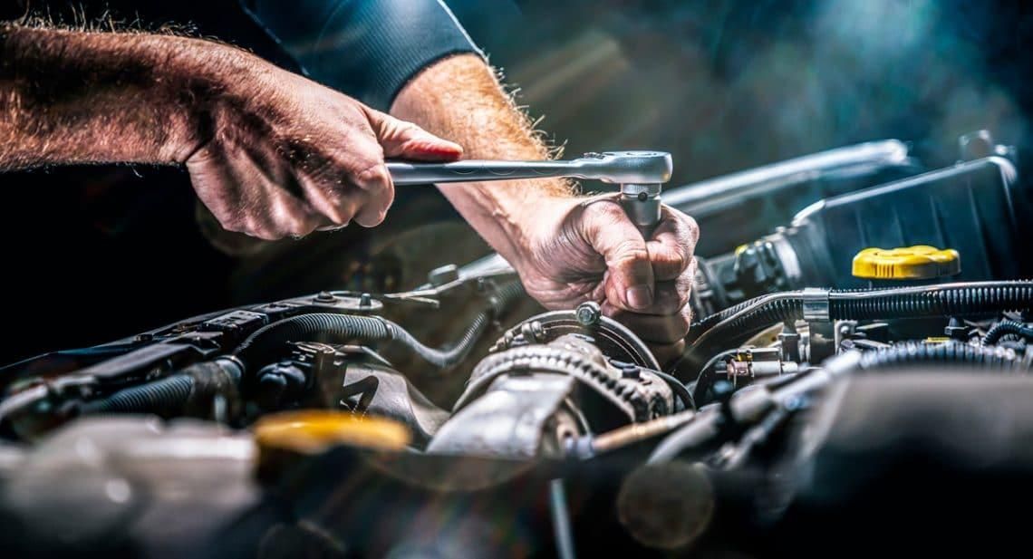 Un mécanicien utilisant une clé pour réparer le moteur ouvert d’une voiture dans un garage sombre