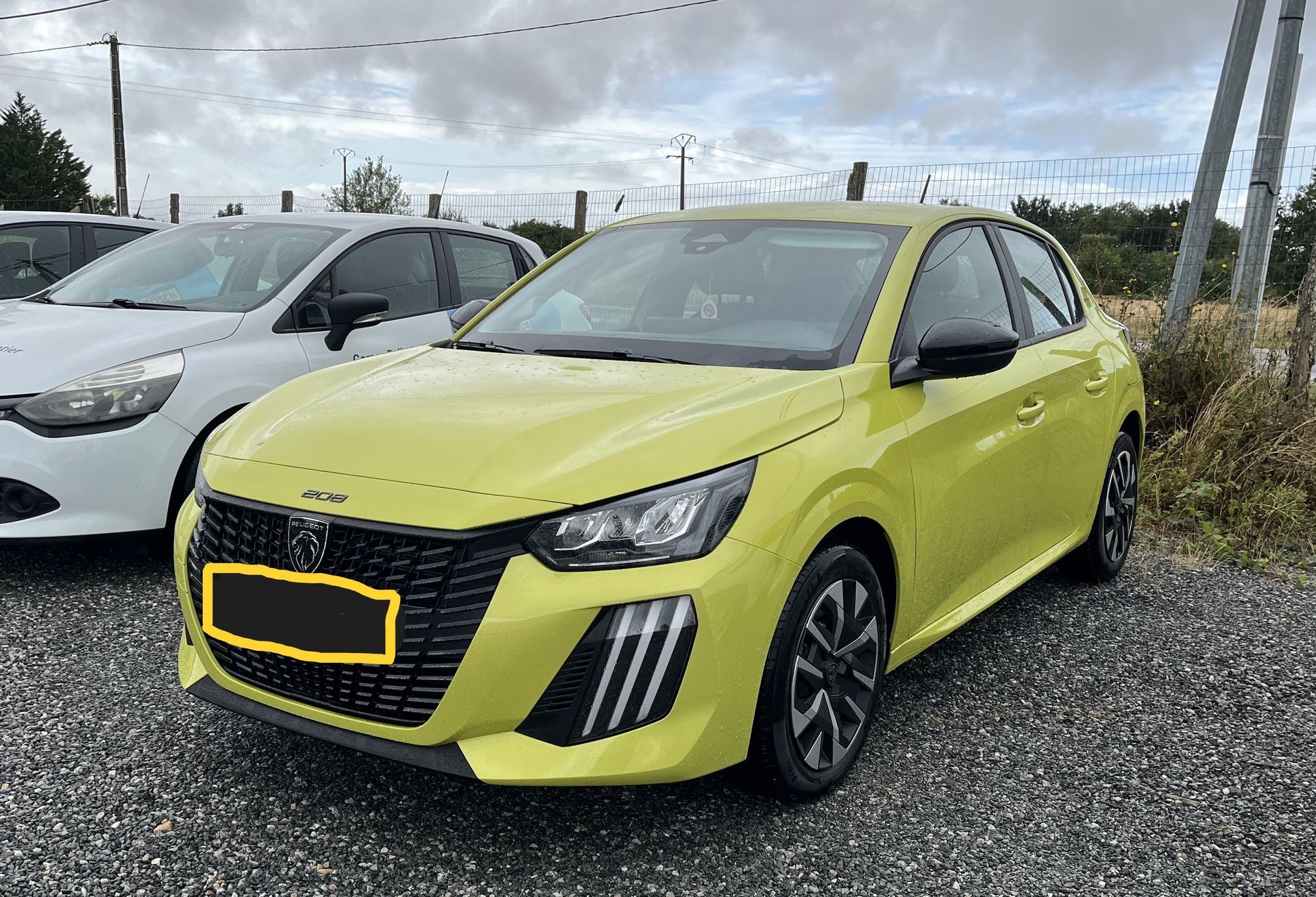Voiture à hayon jaune garée sur un parking en gravier, à côté d’une voiture blanche