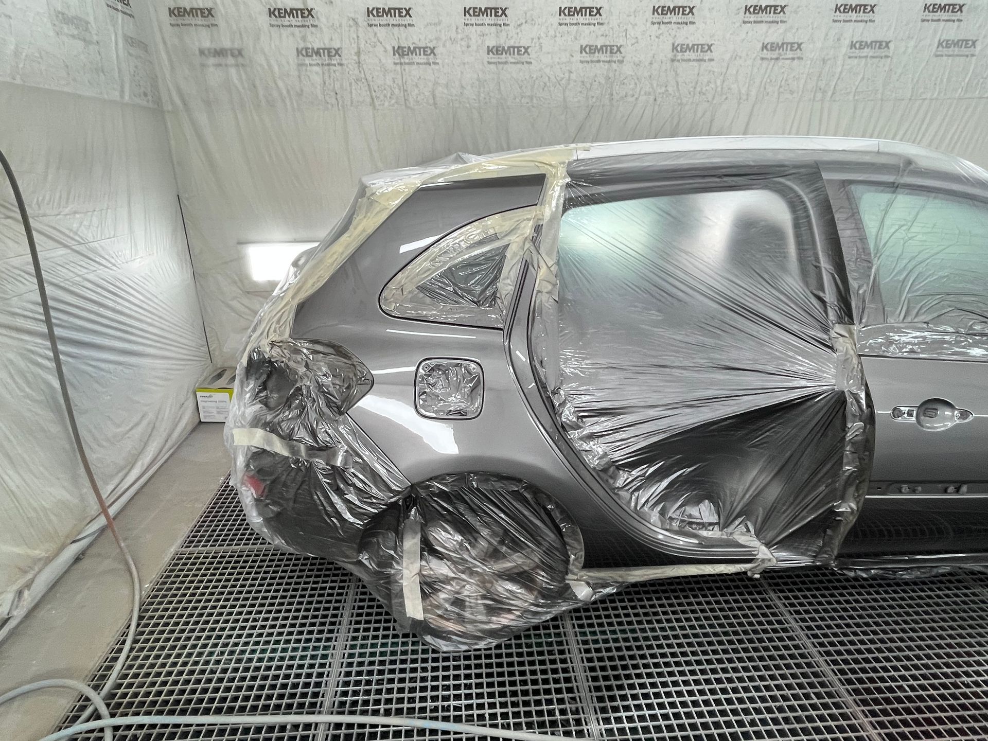 SUV gris endommagé dans une cabine de peinture, avec l’arrière enfoncé et une roue abîmée