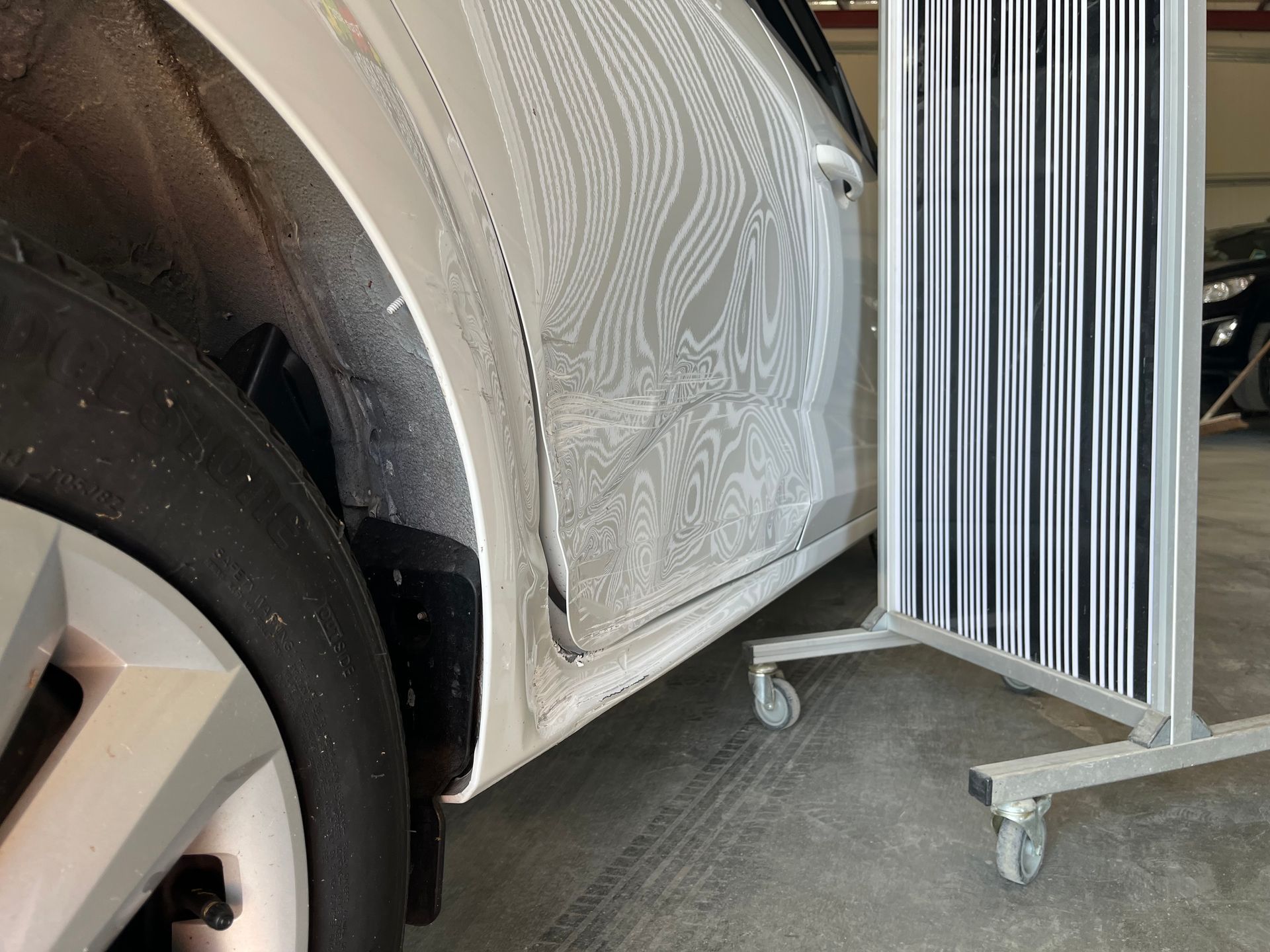 Panneau latéral de voiture en cours de covering avec un film gris à motifs, à côté d’un présentoir roulant chargé de matériaux