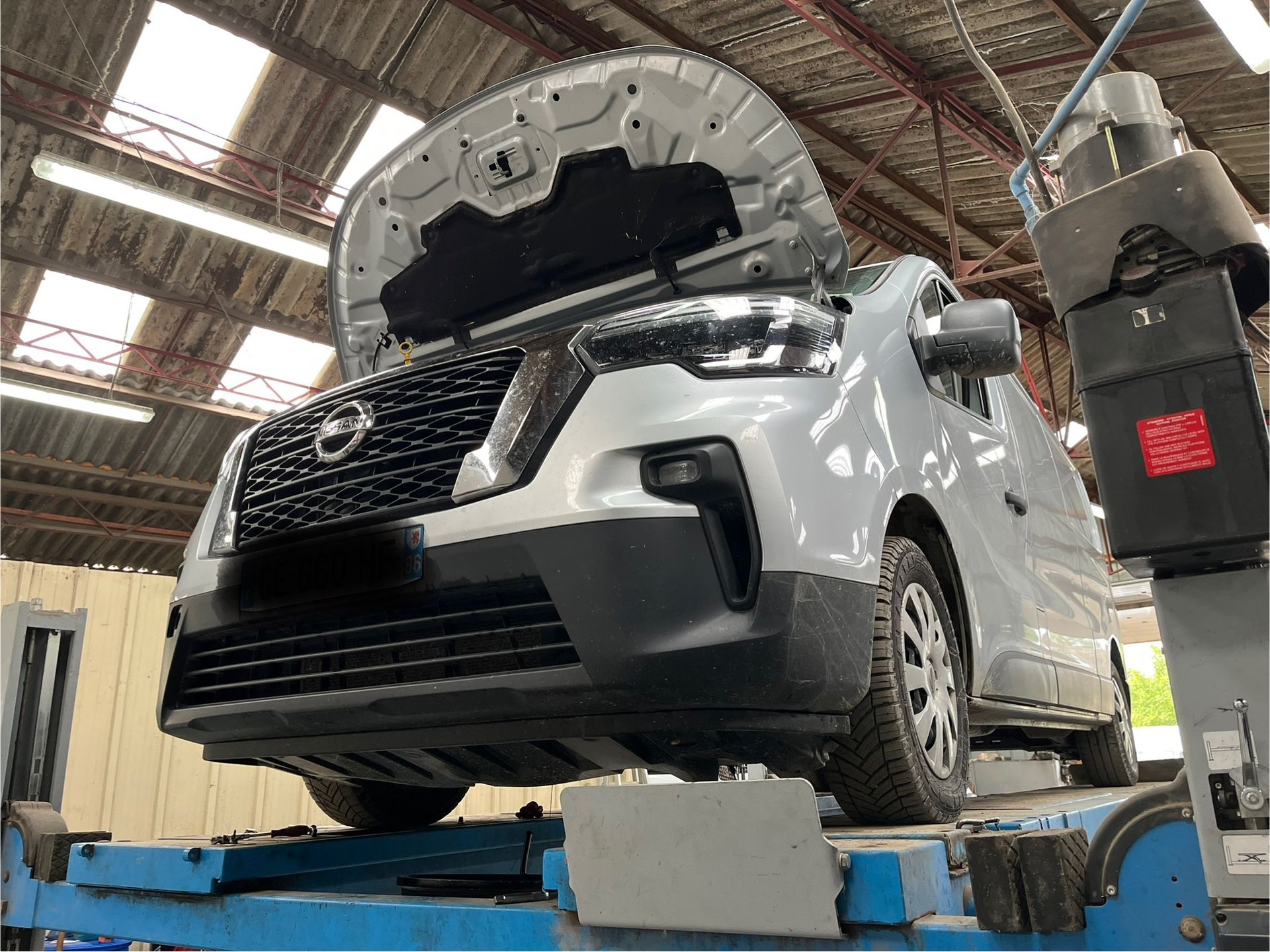 SUV blanc sur un pont élévateur dans un garage automobile, capot ouvert pour inspection