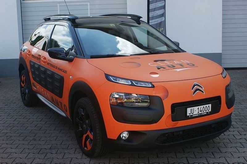 Une citroen c4 cactus orange est garée devant une porte de garage
