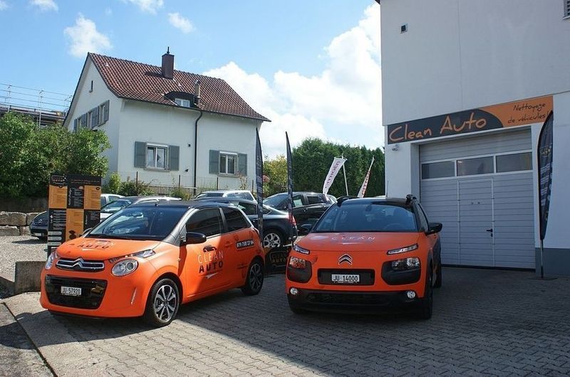 Deux voitures oranges sont garées devant un garage automobile propre