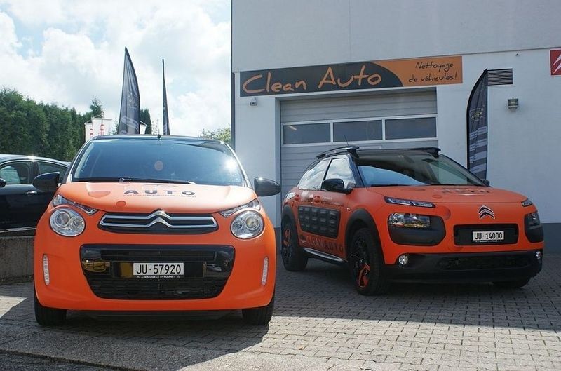 Deux voitures oranges sont garées devant un magasin de voitures propres