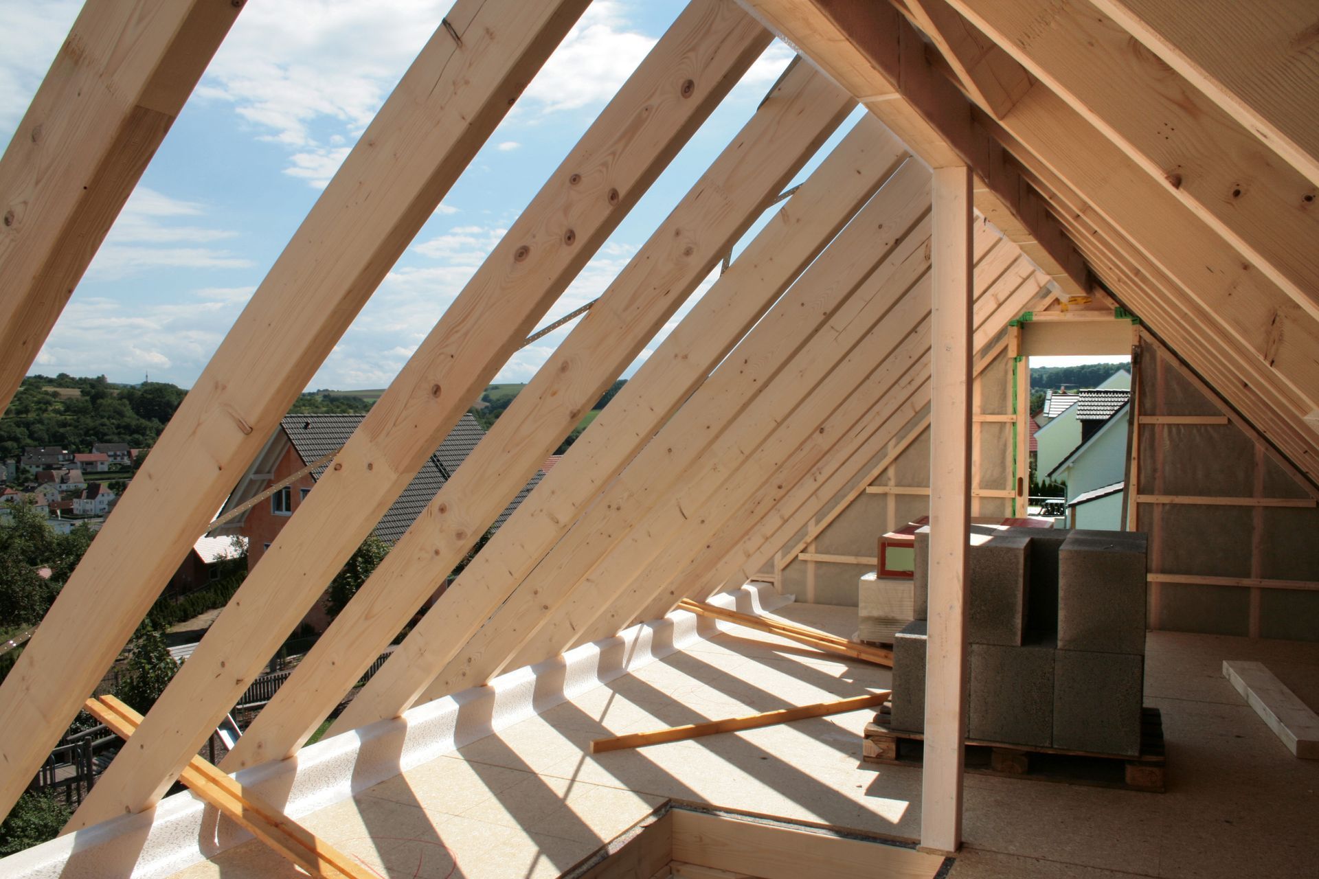 Construction d'une charpente de combles en bois avec chevrons apparents et vue sur la ville à travers une partie ouverte du toit.