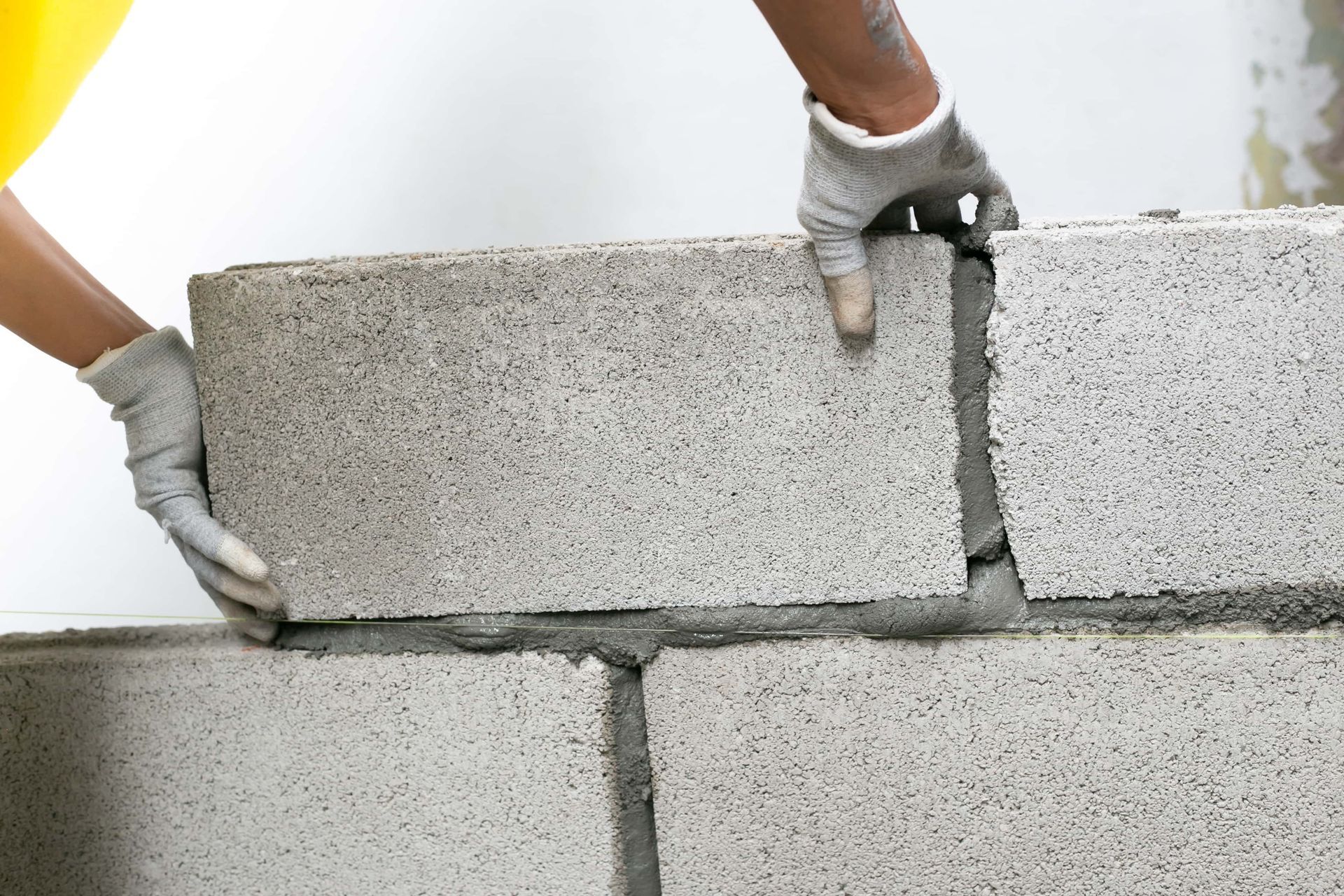 Des mains gantées posent un mur en parpaings gris avec du mortier frais