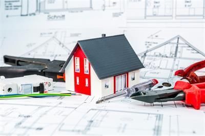 Ein Modellhaus steht auf einem Bauplan neben Werkzeugen.