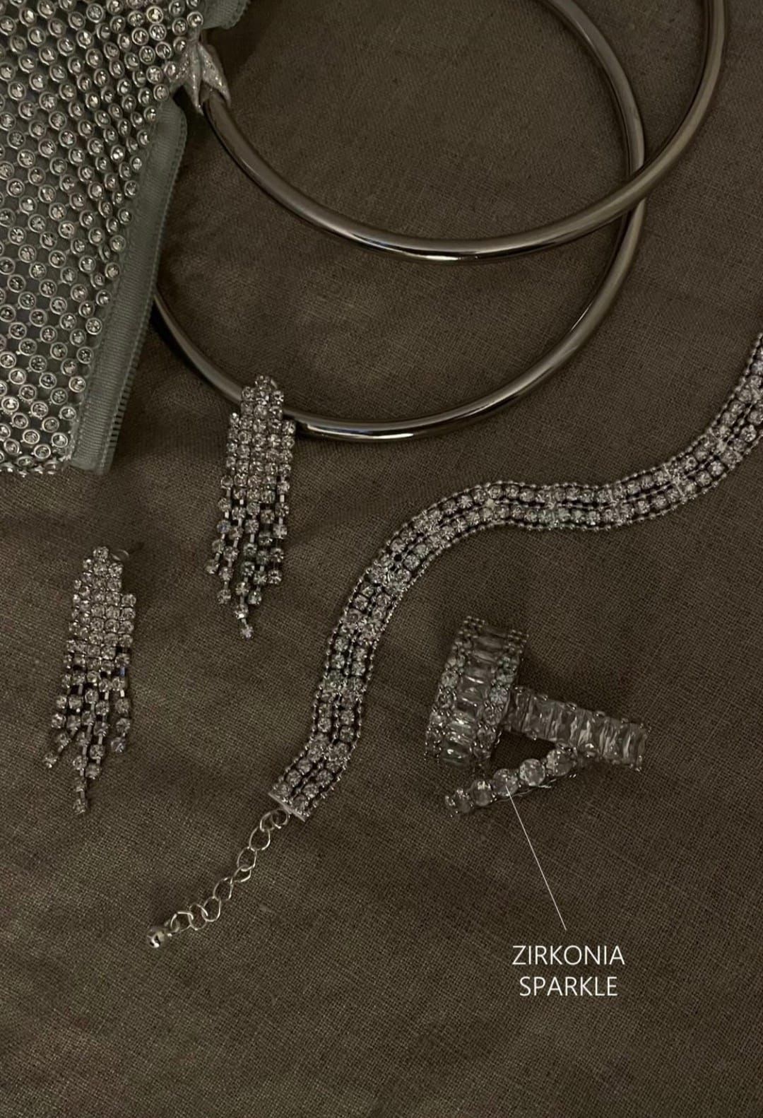 Conjunto de joyas en tela oscura. Incluye collar, pendientes, pulsera y anillo, todos adornados con circonitas brillantes.