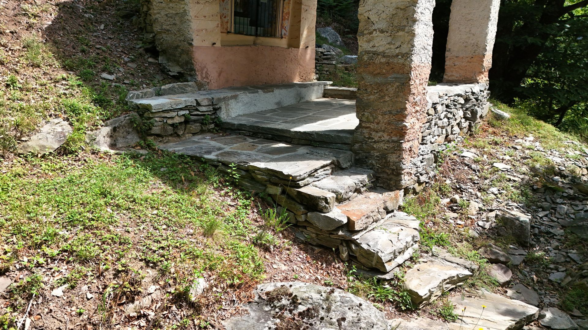 Un sentiero tortuoso in pietra che attraversa un'area verde e boscosa, con rive erbose su entrambi i lati.
