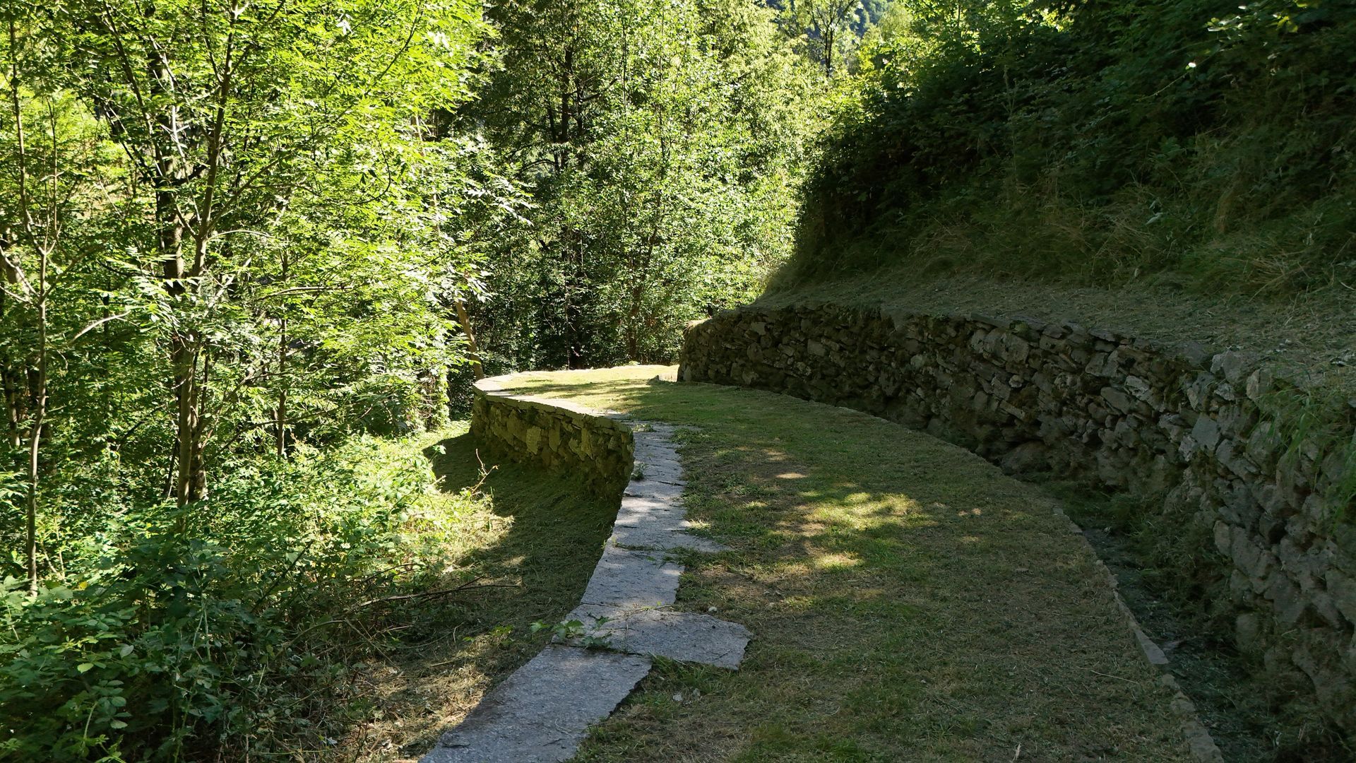 Un piccolo santuario bianco costruito su una parete rocciosa, con un tetto in pietra e una piccola ringhiera in ferro.