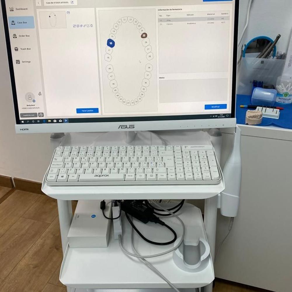 Un monitor de computadora está colocado encima de un estante blanco al lado de un teclado.