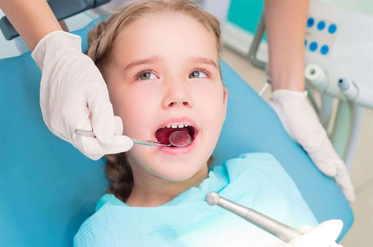 A una niña le están examinando los dientes un dentista.