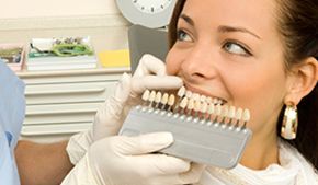 Una mujer está sentada en una silla dental sosteniendo una tabla de colores de dientes.