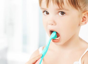 Una niña se cepilla los dientes con un cepillo de dientes azul.