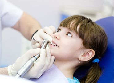 A una niña le están examinando los dientes un dentista.
