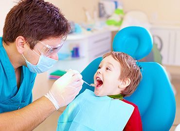 Un niño pequeño está sentado en una silla dental mientras un dentista le examina los dientes.