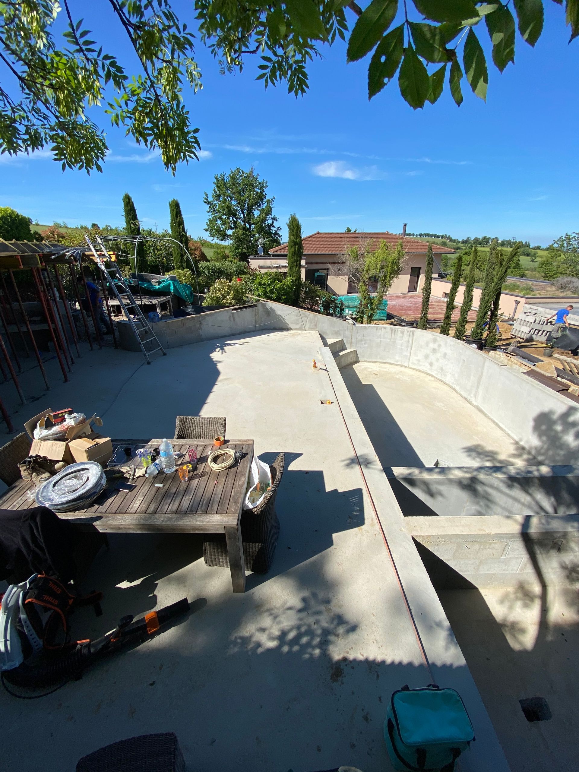 Piscine en béton en construction, avec outils et environnement résidentiel. Journée ensoleillée.