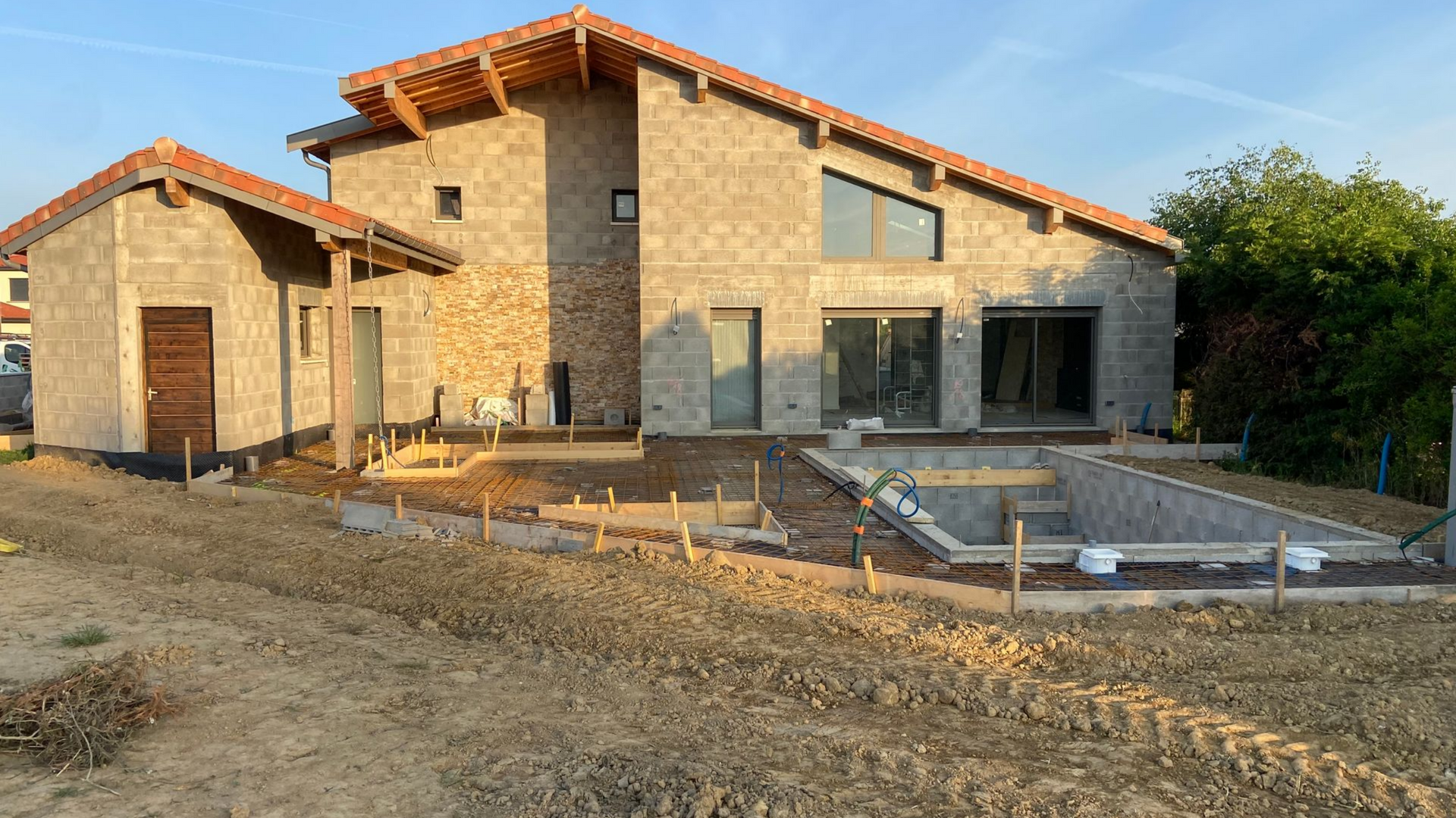 Une maison en construction avec piscine, entourée de terre et de matériaux de construction, baignée de soleil.