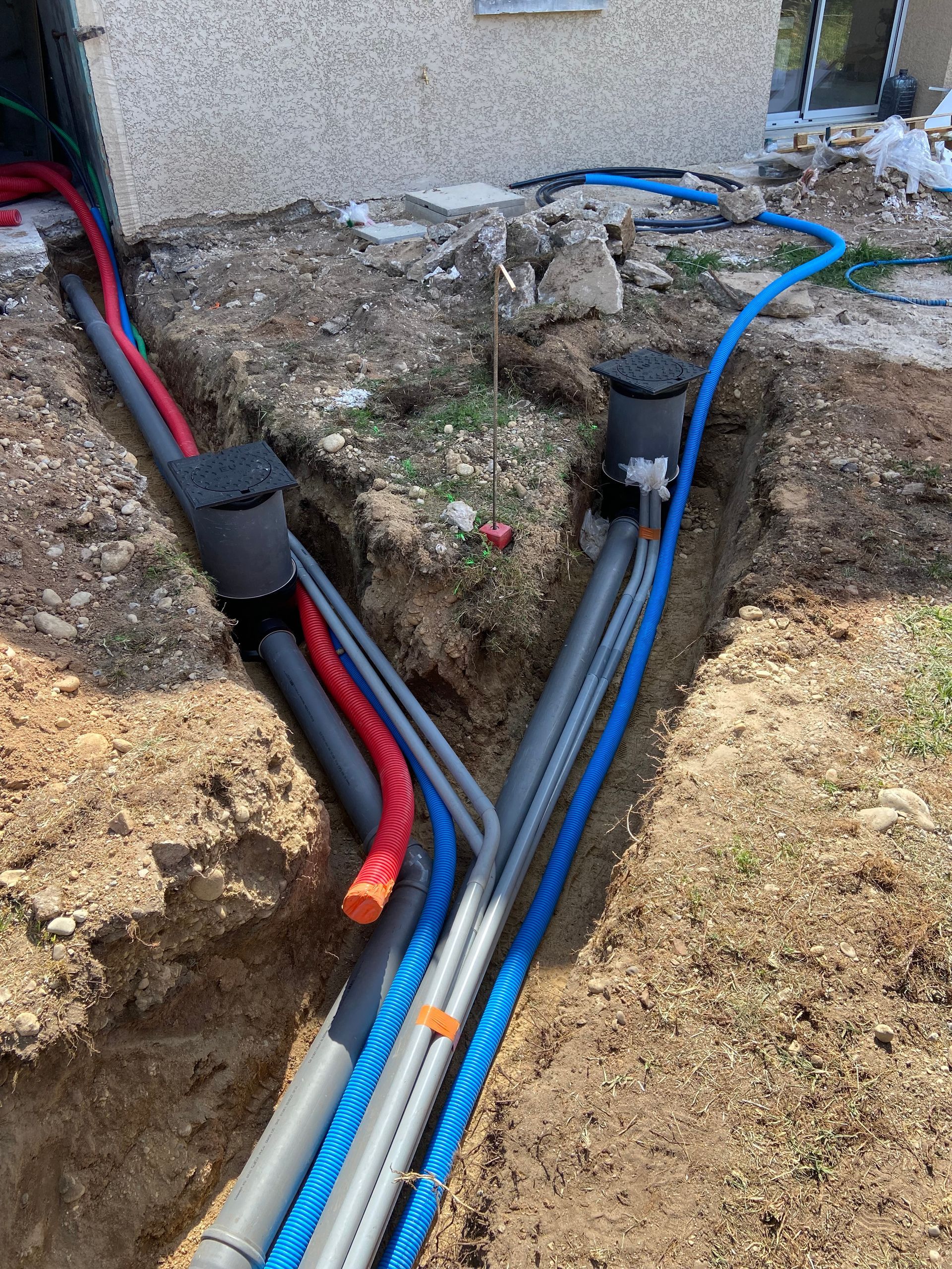 Des canalisations électriques et de plomberie enterrées mènent aux fondations du bâtiment. On distingue des conduits de différentes couleurs et des points d'accès.