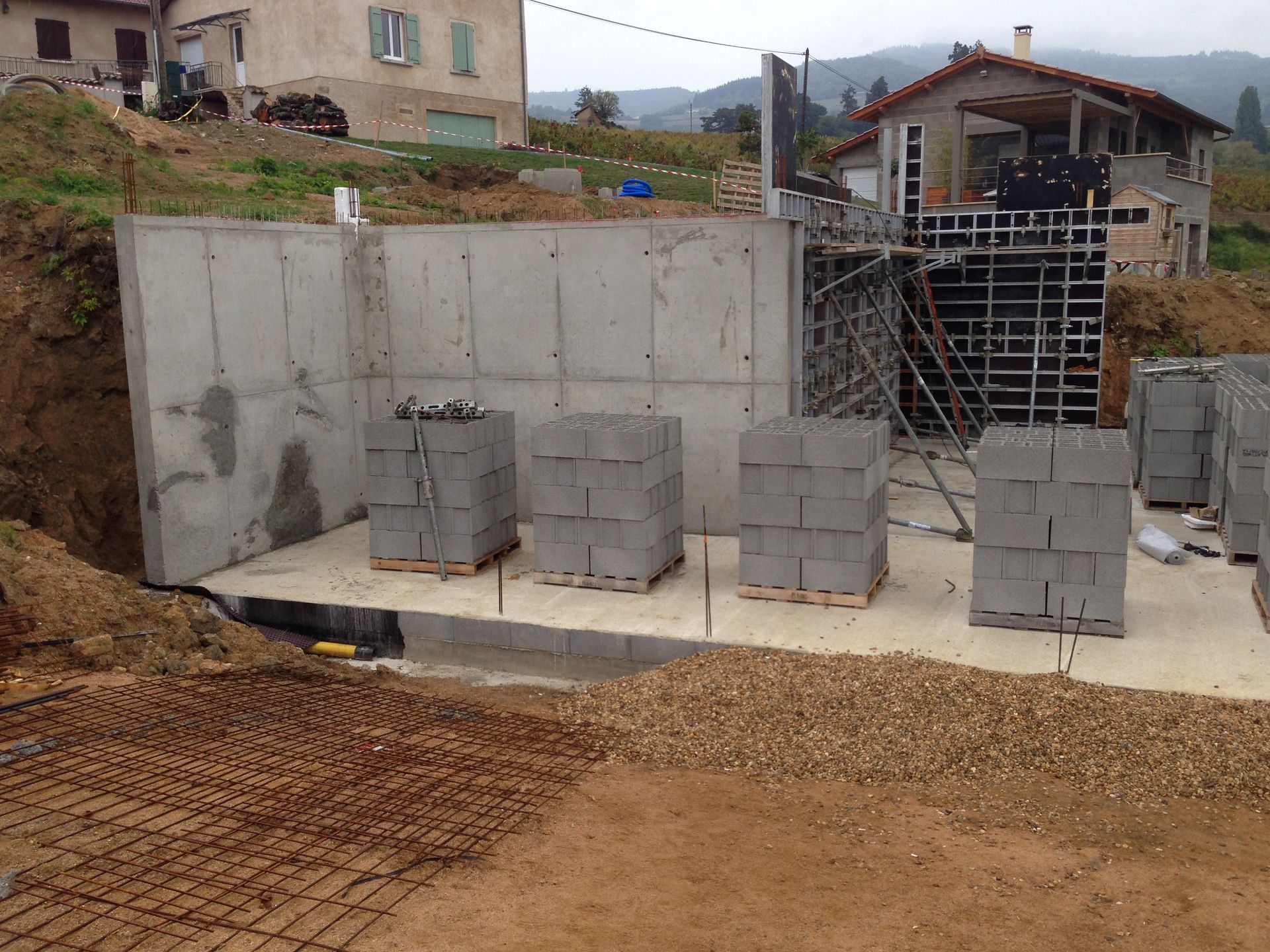 Chantier de construction avec murs en béton, parpaings et treillis d'armature.