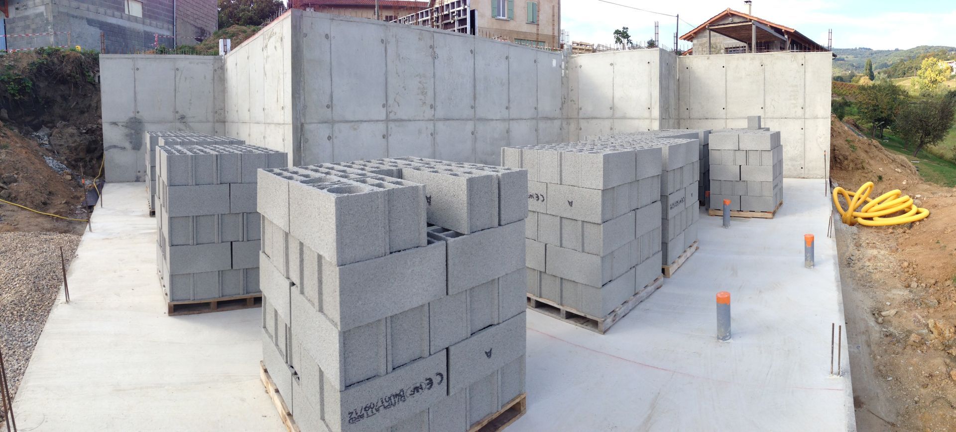 Chantier de construction avec des murs en béton et des piles de parpaings gris.