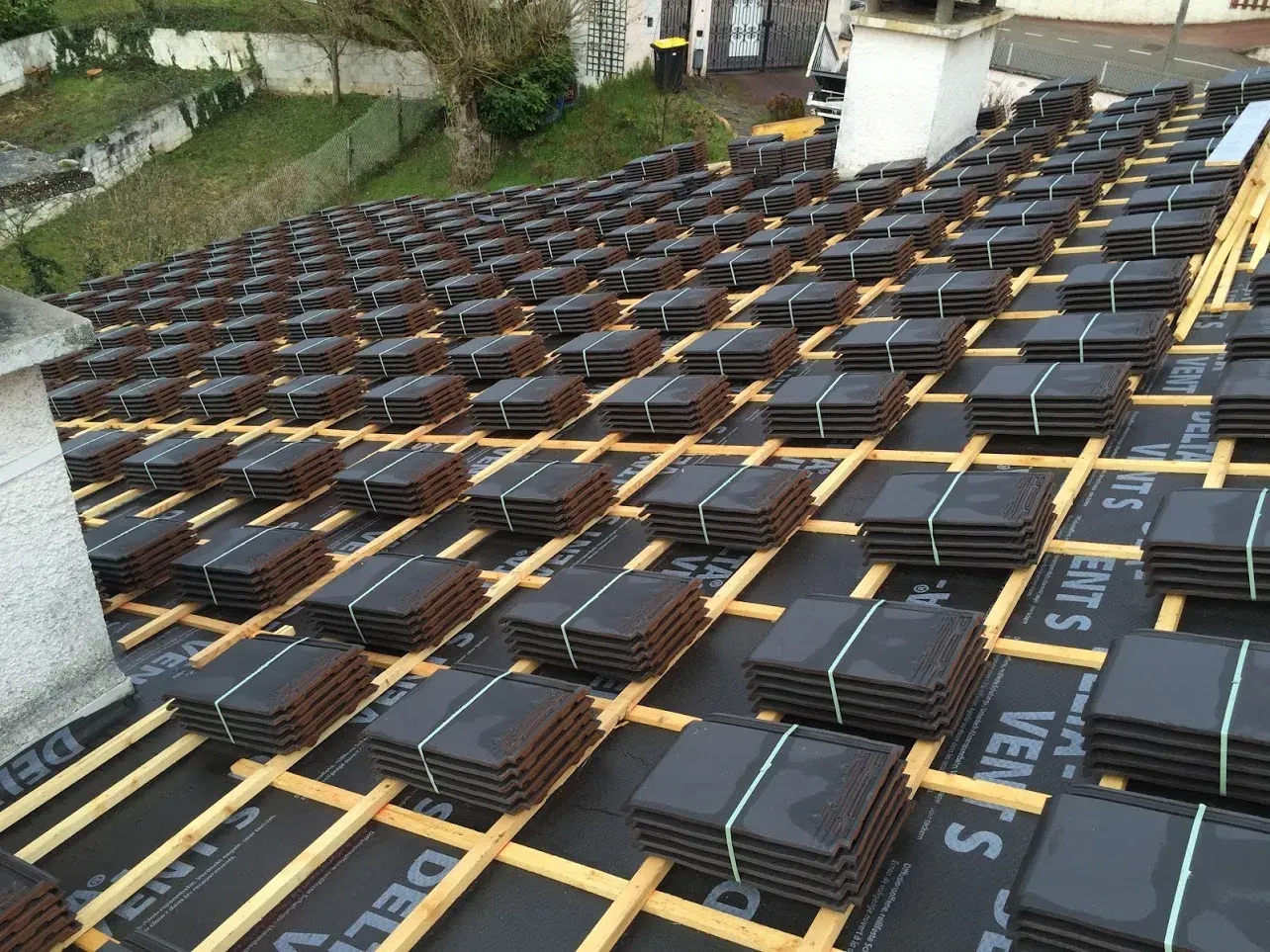 Toiture composée de paquets de tuiles sombres empilés sur des supports en bois.