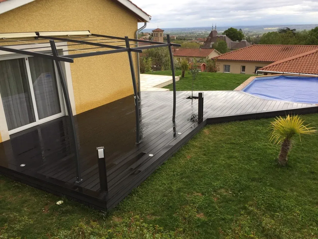 Terrasse en bois avec pergola, douche et piscine dans un jardin.