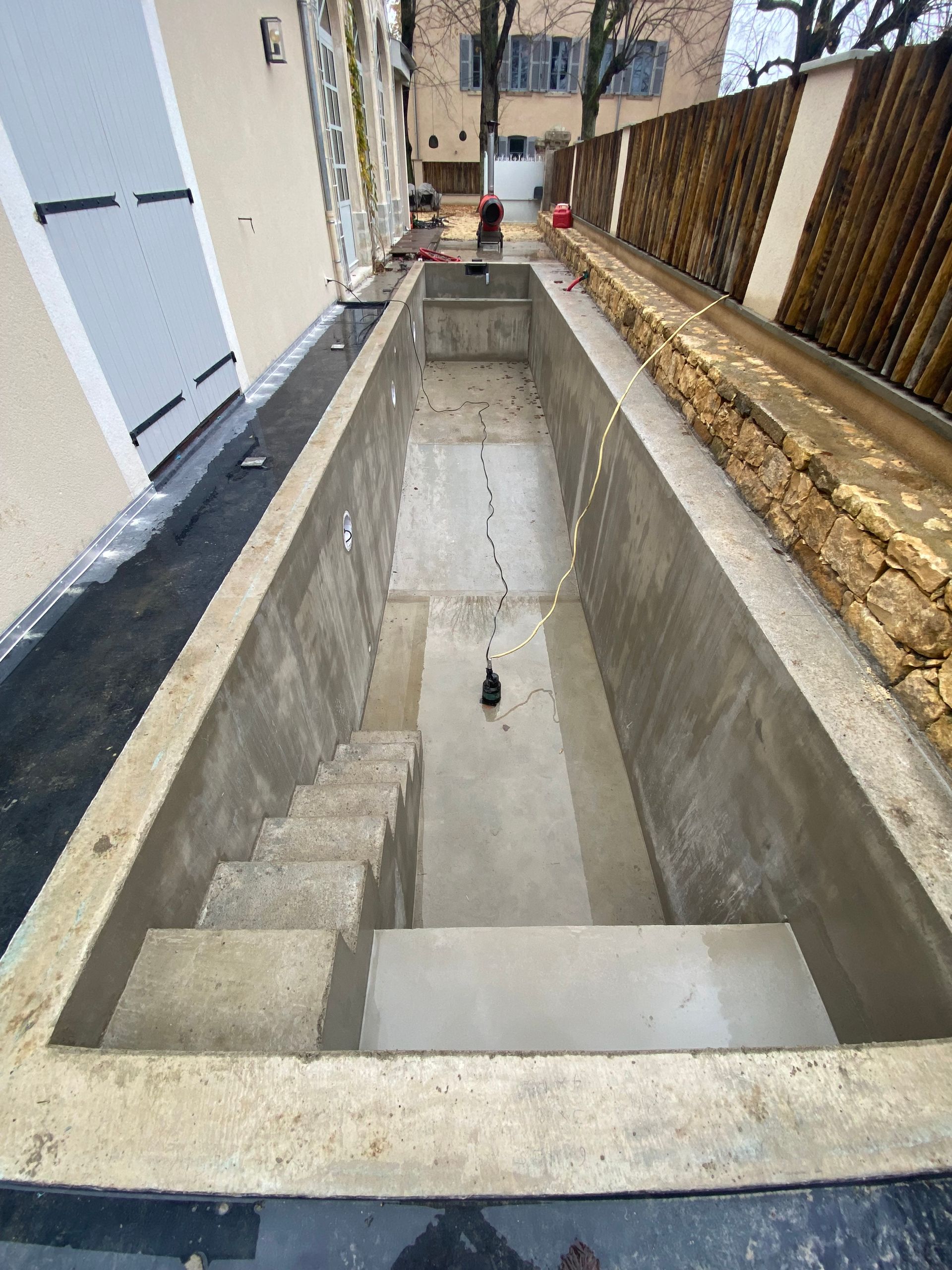 Piscine rectangulaire en béton en construction avec escalier, cour latérale étroite.