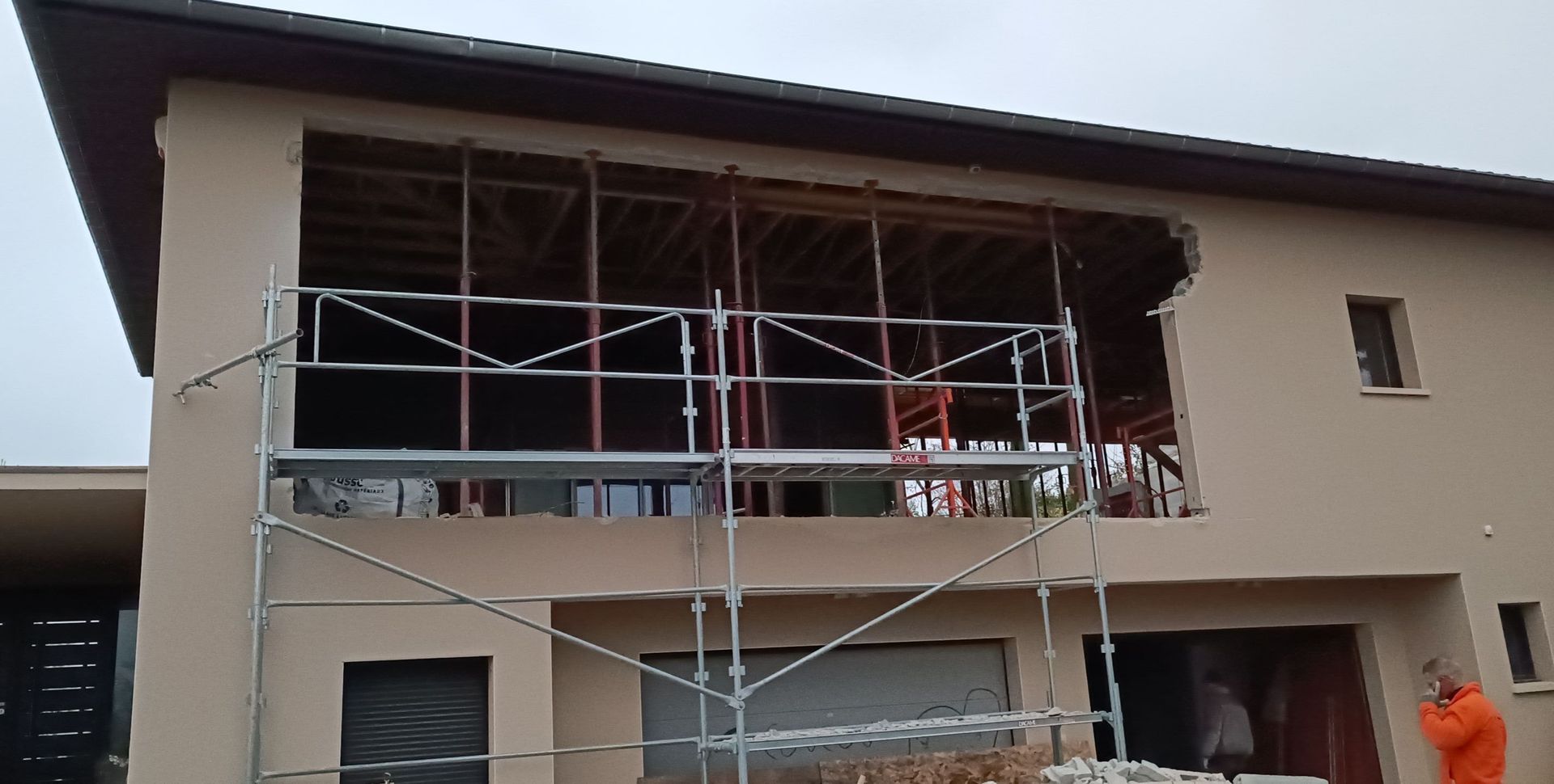 Extérieur de la maison en construction, avec des échafaudages et une grande ouverture pour une fenêtre ou une porte.