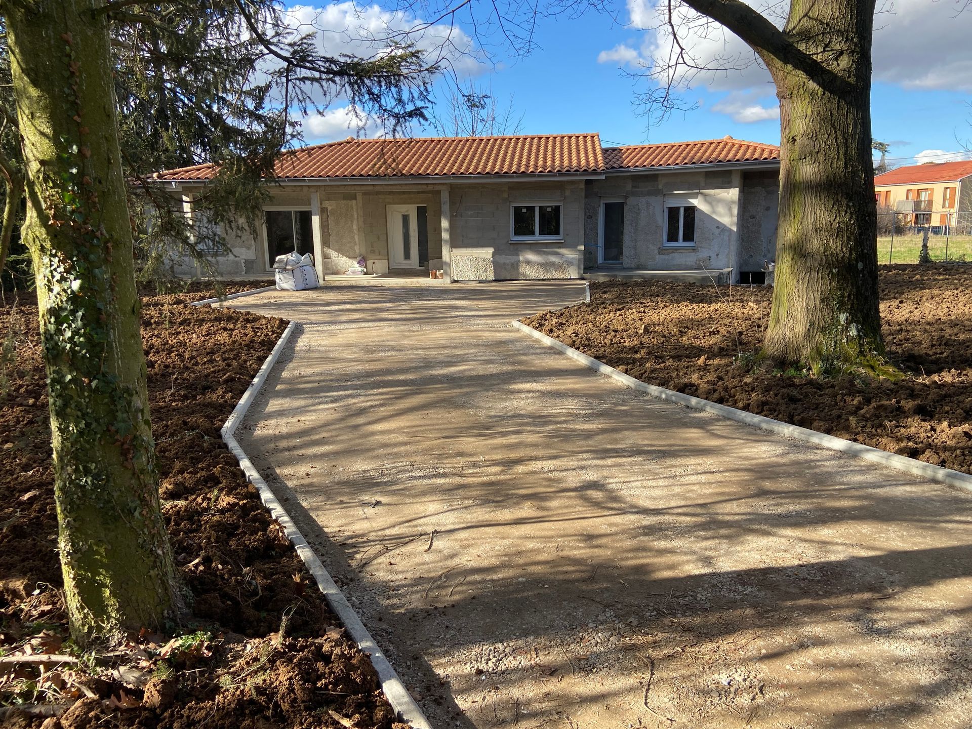 Une maison de plain-pied avec un chemin de gravier menant à la porte d'entrée. Des arbres bordent le chemin.