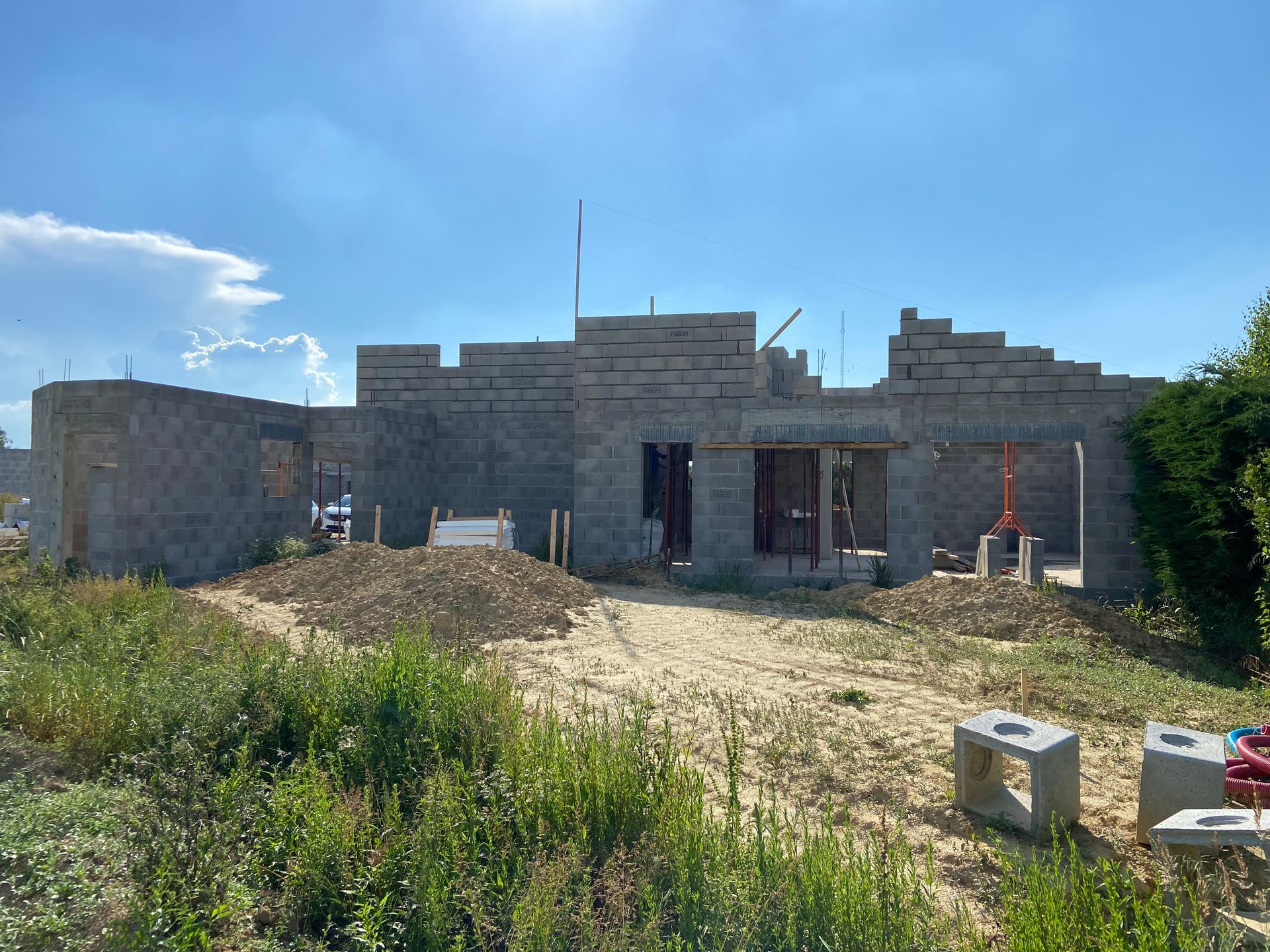 Chantier : bâtiment en parpaings gris partiellement construit par une journée ensoleillée.