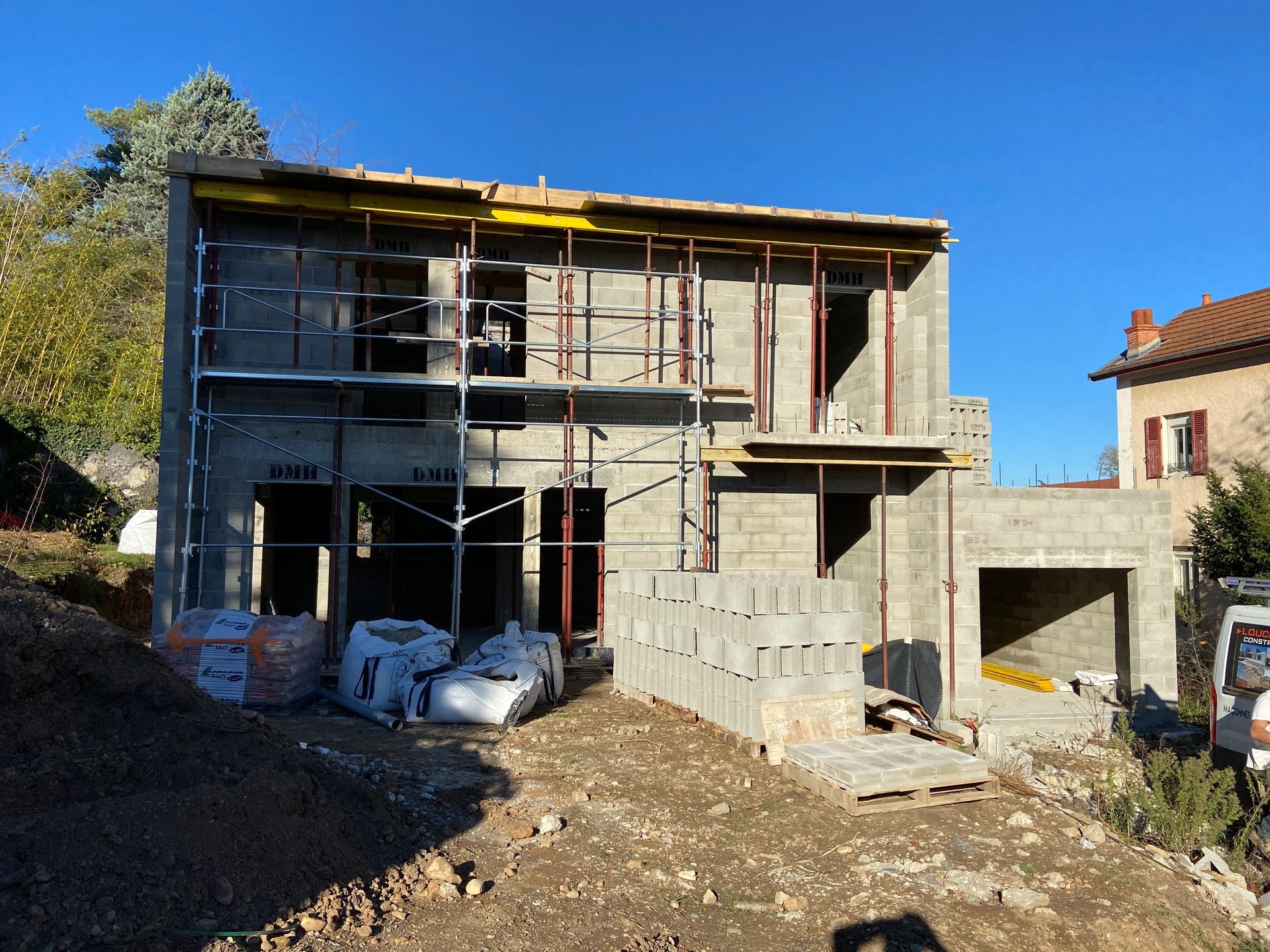 Maison à deux étages en construction, parpaings gris, échafaudages, ciel dégagé.