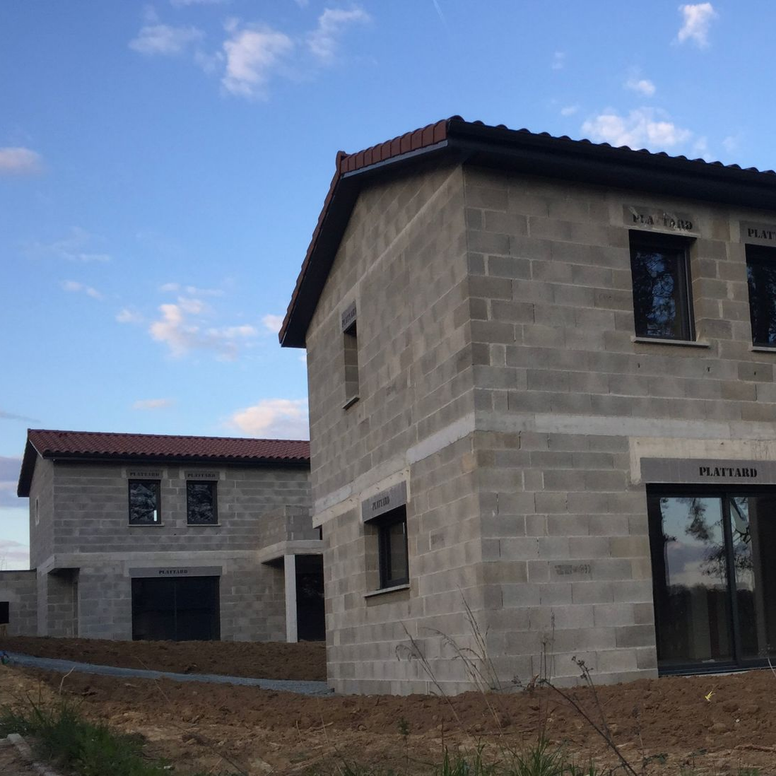 Deux maisons inachevées en parpaings de béton gris sous un ciel bleu.
