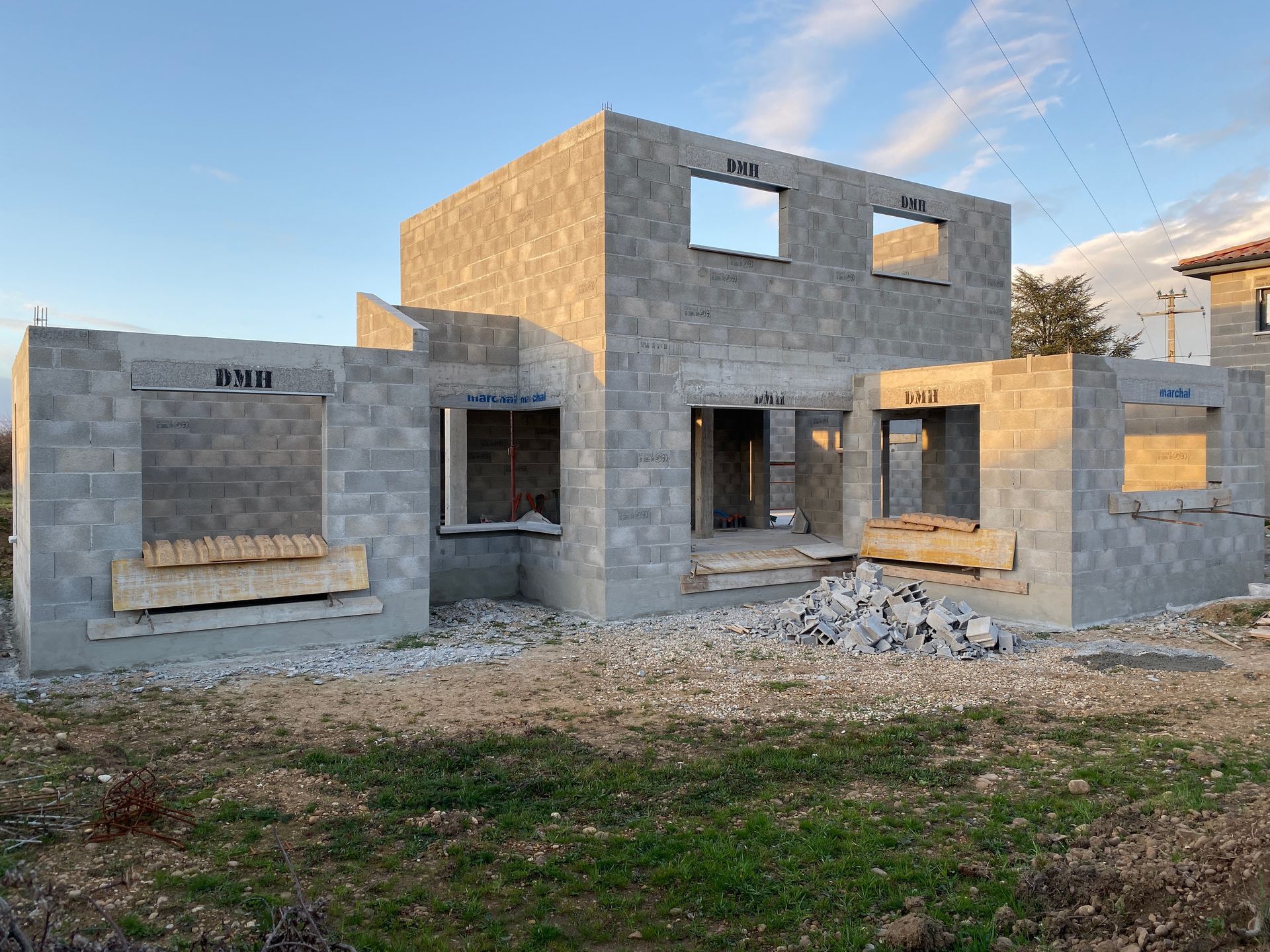 Maison en parpaings de béton en construction, avec des cadres de fenêtres vides, sur un terrain gazonné.