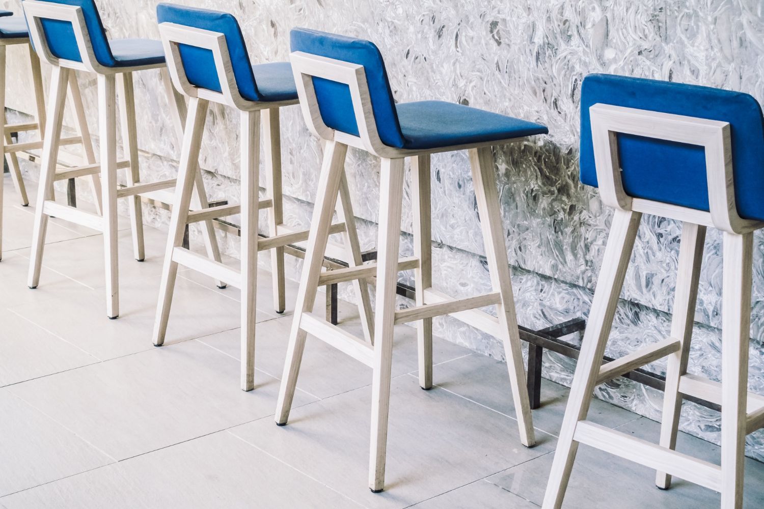 Los taburetes de bar con cojines azules se alinean contra una pared y un piso de color blanco texturizado.