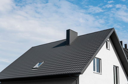 Modernes weißes Haus mit dunkelgrauem Ziegeldach und Oberlicht unter blauem Himmel