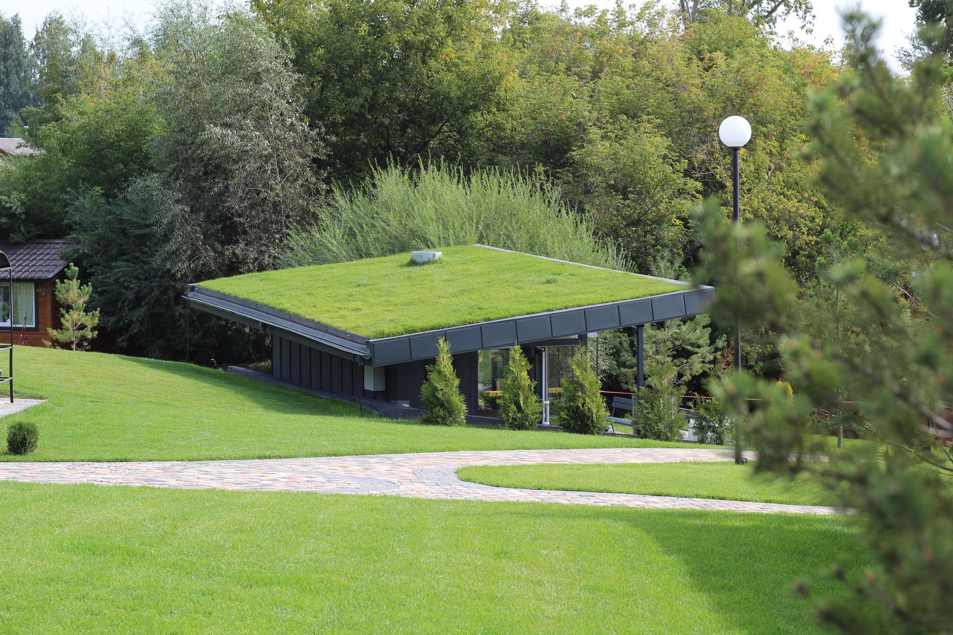 Ein mit Gras gedecktes Haus, eingebettet zwischen Bäumen an einem Weg in einer grünen Parklandschaft
