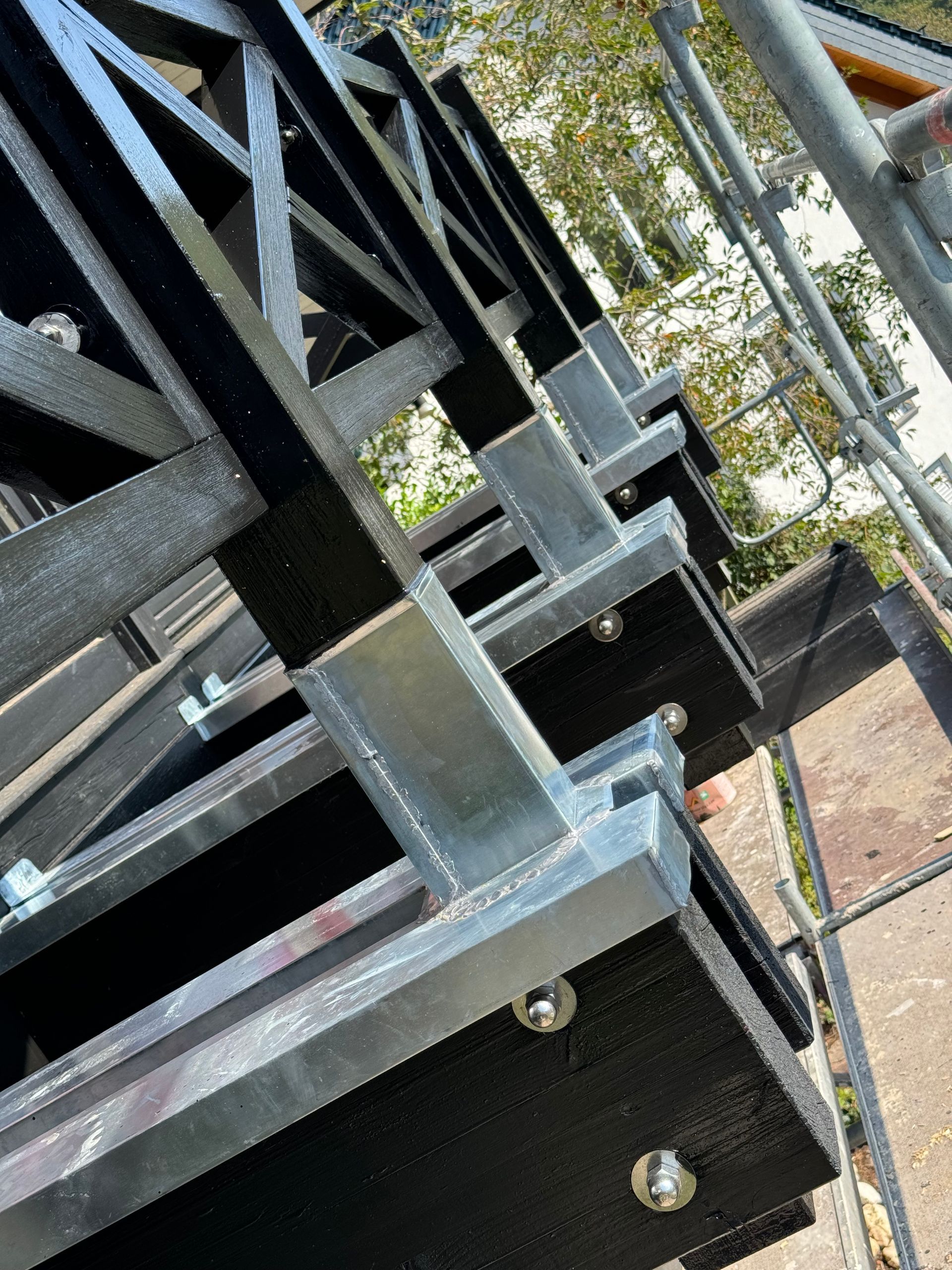 Schwarze Metalltreppe mit Geländern im Freien, von unten vor Bäumen und Himmel betrachtet