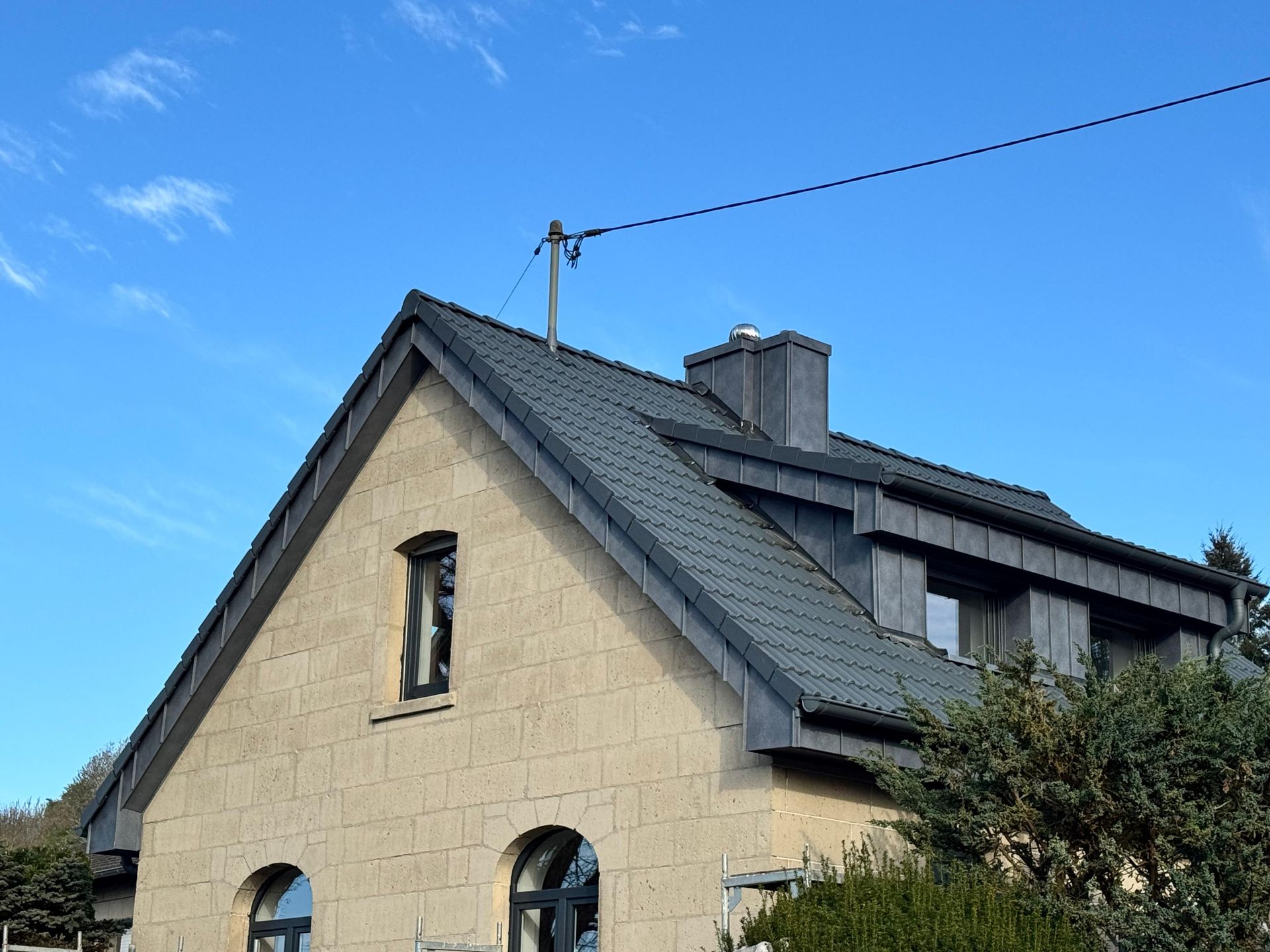 Weißes Haus mit dunkelgrauem Ziegeldach und Oberlicht unter blauem Himmel