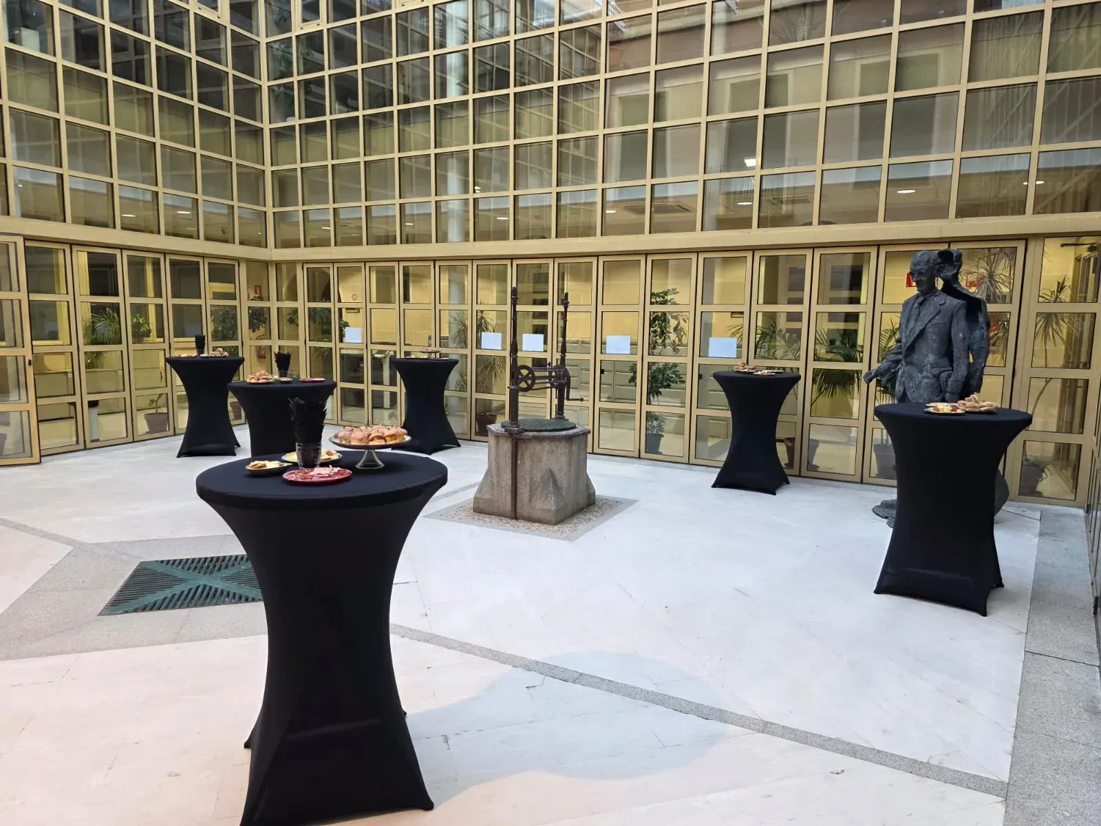 Patio con mesas de cóctel negras preparadas para un evento; un pozo en el centro.