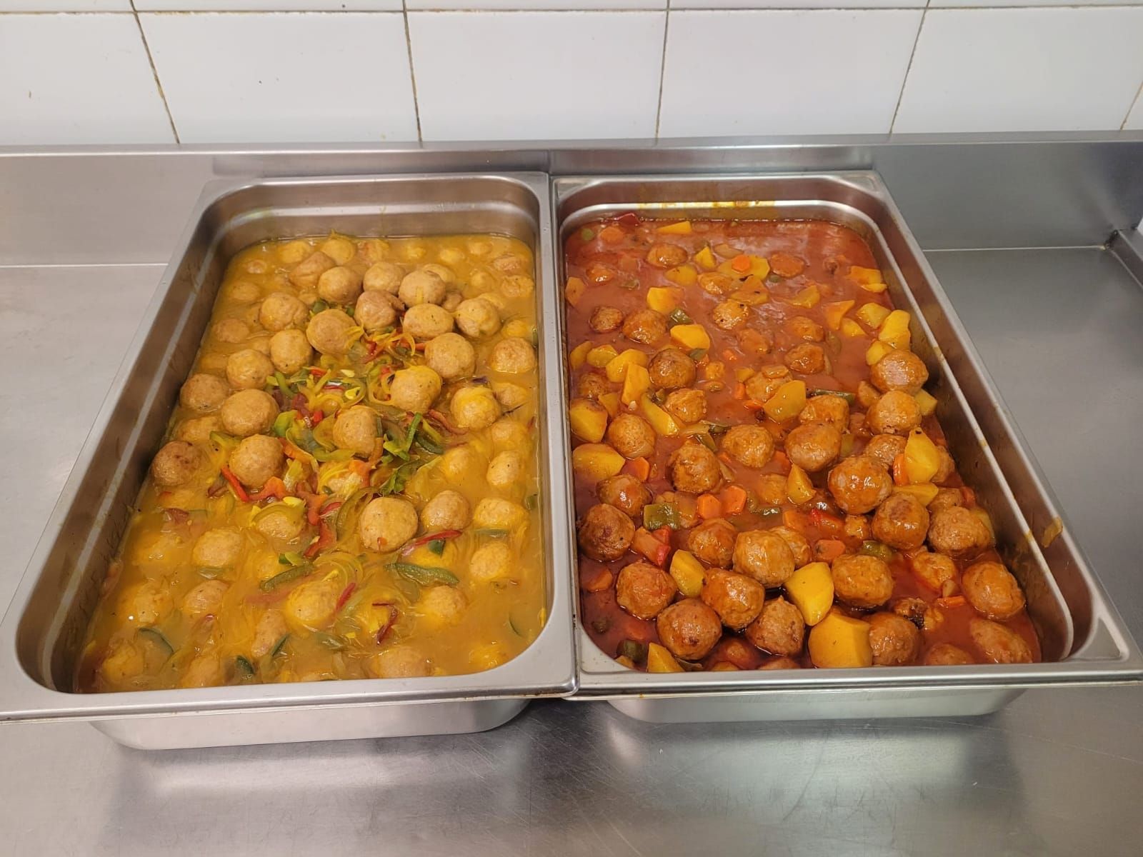 Dos bandejas de metal con albóndigas guisadas en diferentes salsas; una amarilla y otra roja.