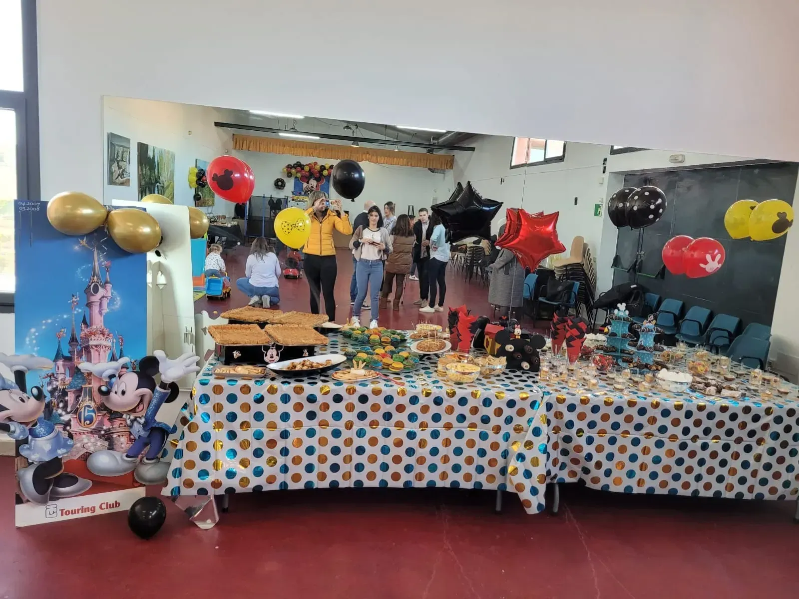 Escena de fiesta: Mesas con bocadillos, decoraciones de Disney, globos y personas en una habitación con un espejo.