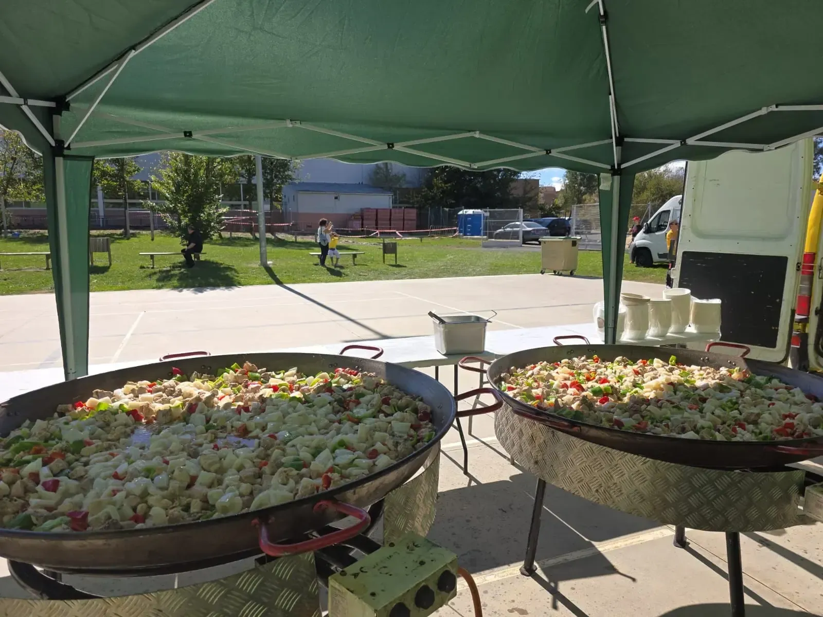 Dos grandes paellas bajo una carpa verde, en un entorno al aire libre.