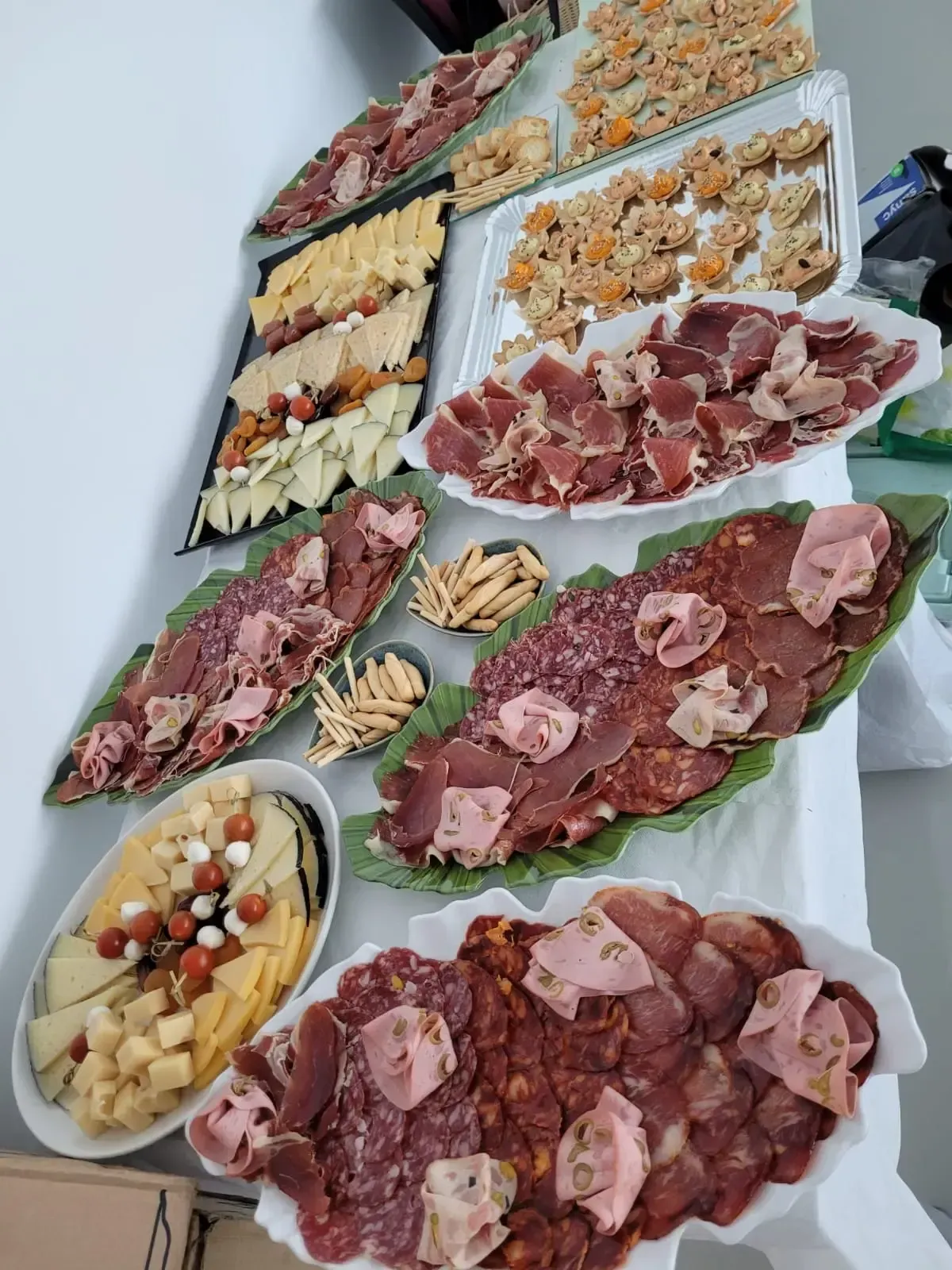 Tabla de embutidos con quesos, carnes, galletas y snacks dispuestos sobre una mesa blanca.