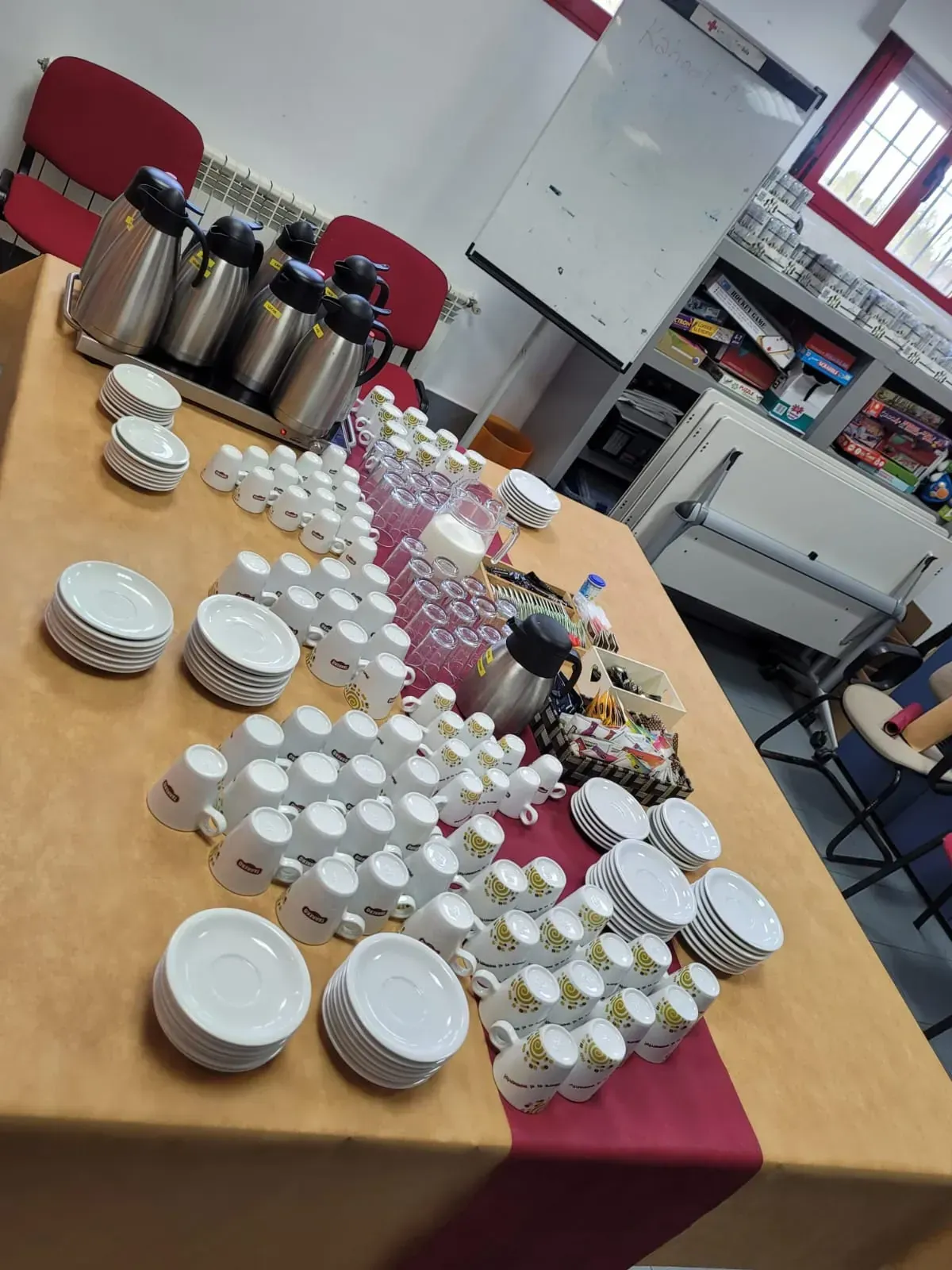 Estación de café y té dispuesta sobre una mesa con tazas, platillos, termos y vasos de agua.