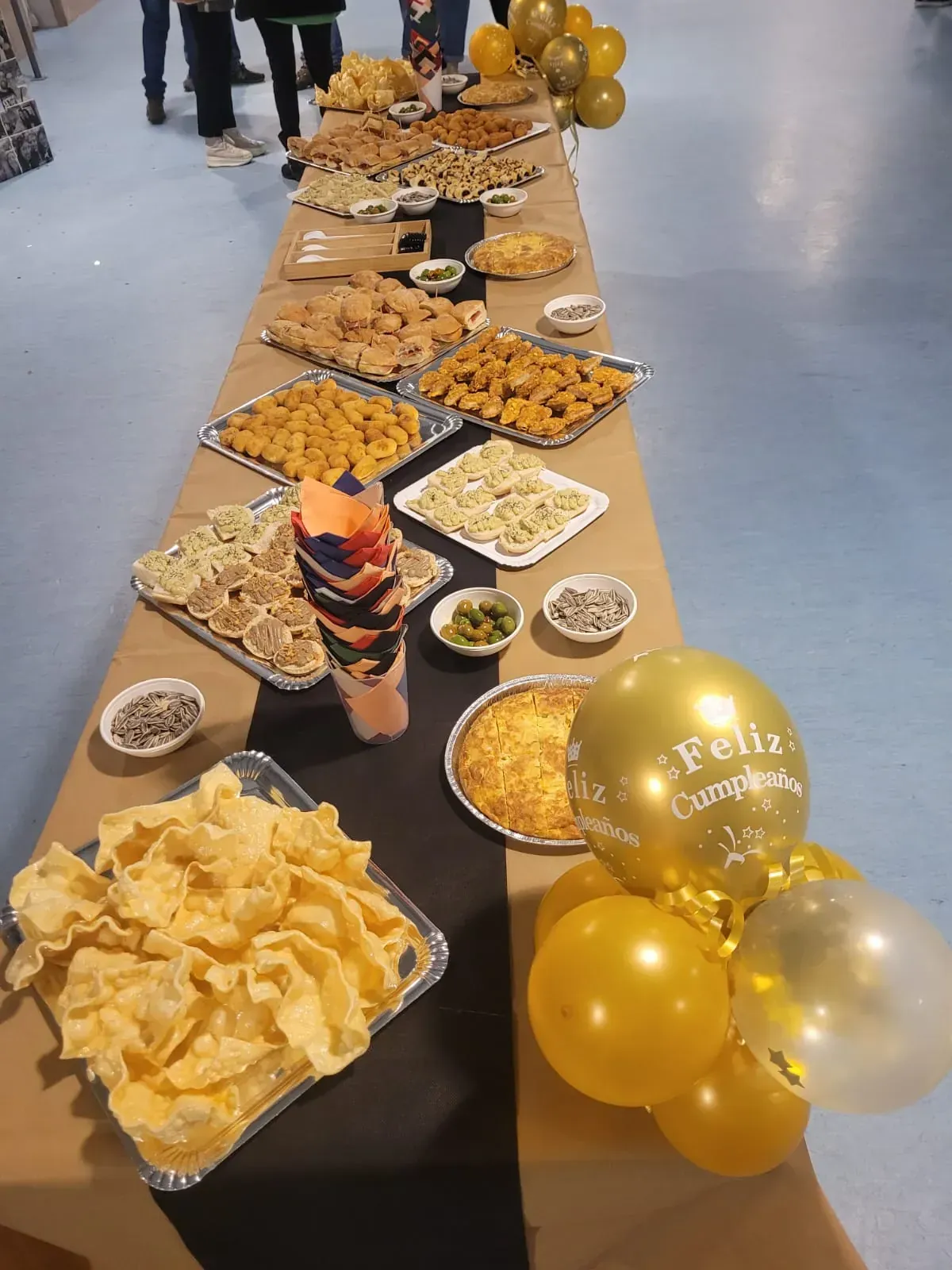 Larga mesa buffet con comida, incluidos aperitivos, globos dorados que dicen